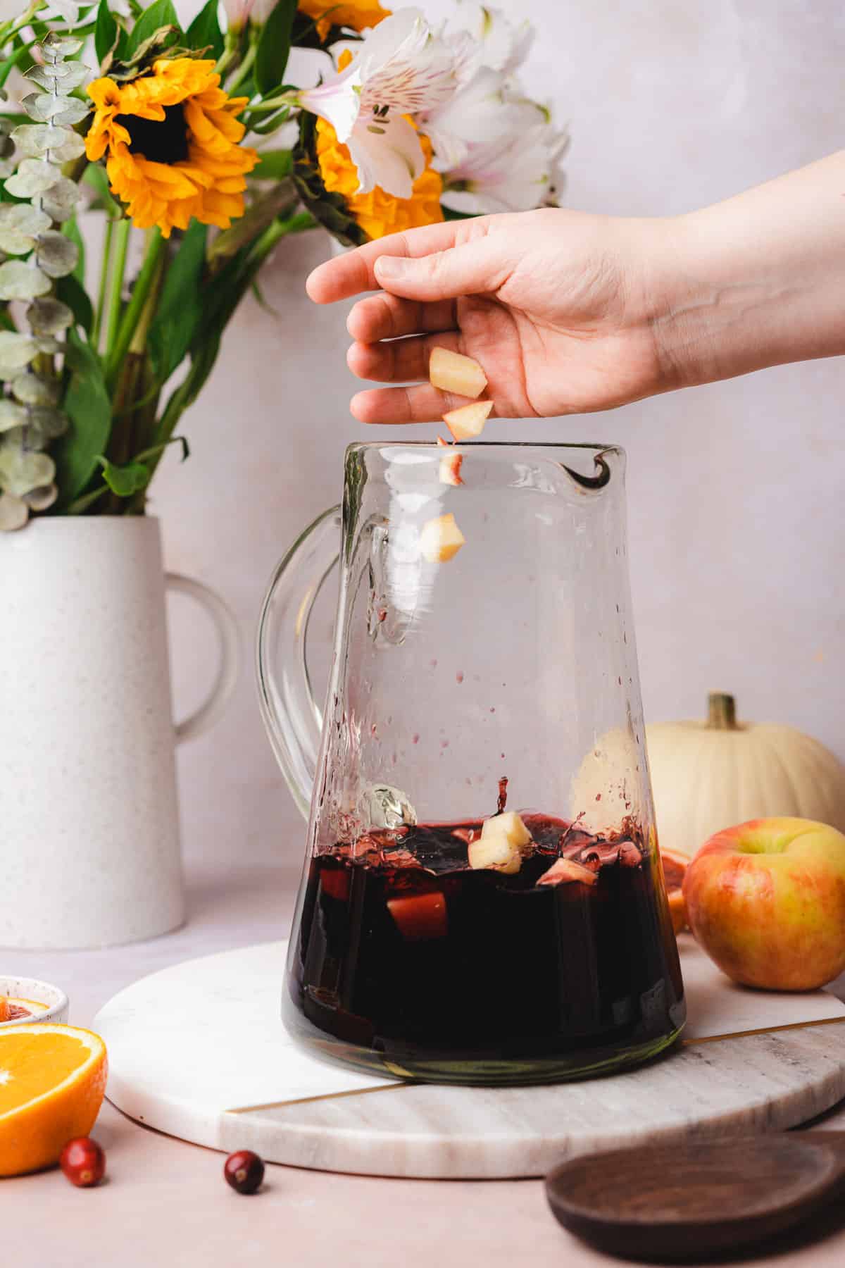 hand dropping apples into a red wine sangria