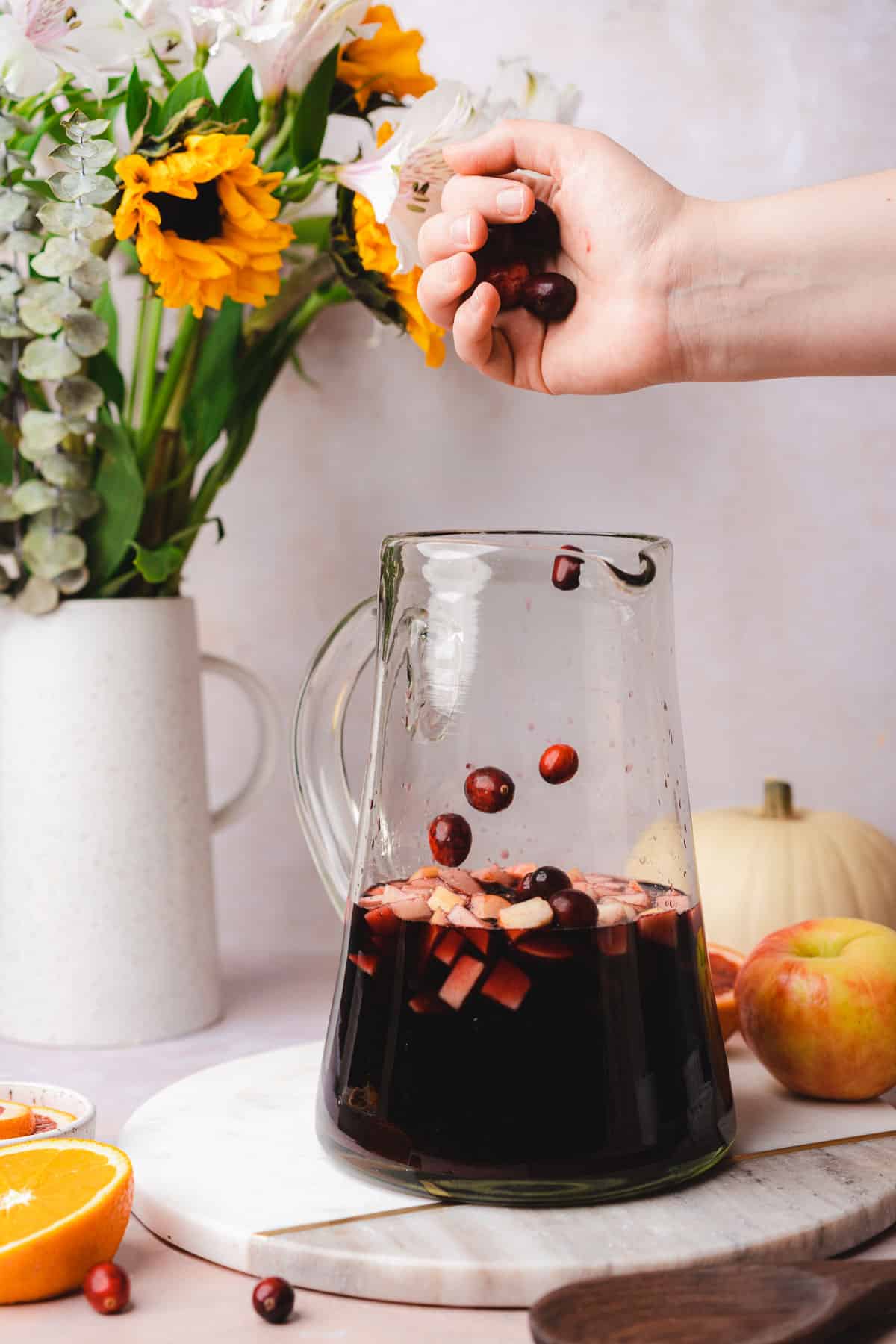 pouring cranberries into a large sangria pitcher