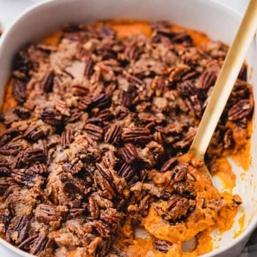 casserole dish of gluten free sweet potato casserole with a scoop taken out so you can see the inside and the pecan praline topping