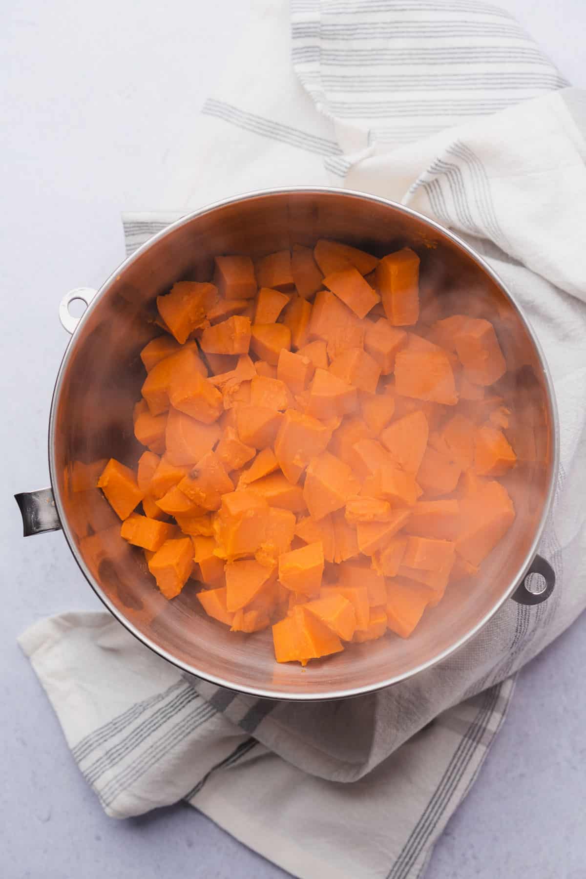 steaming sweet potato cubes in a metal mixing bowl