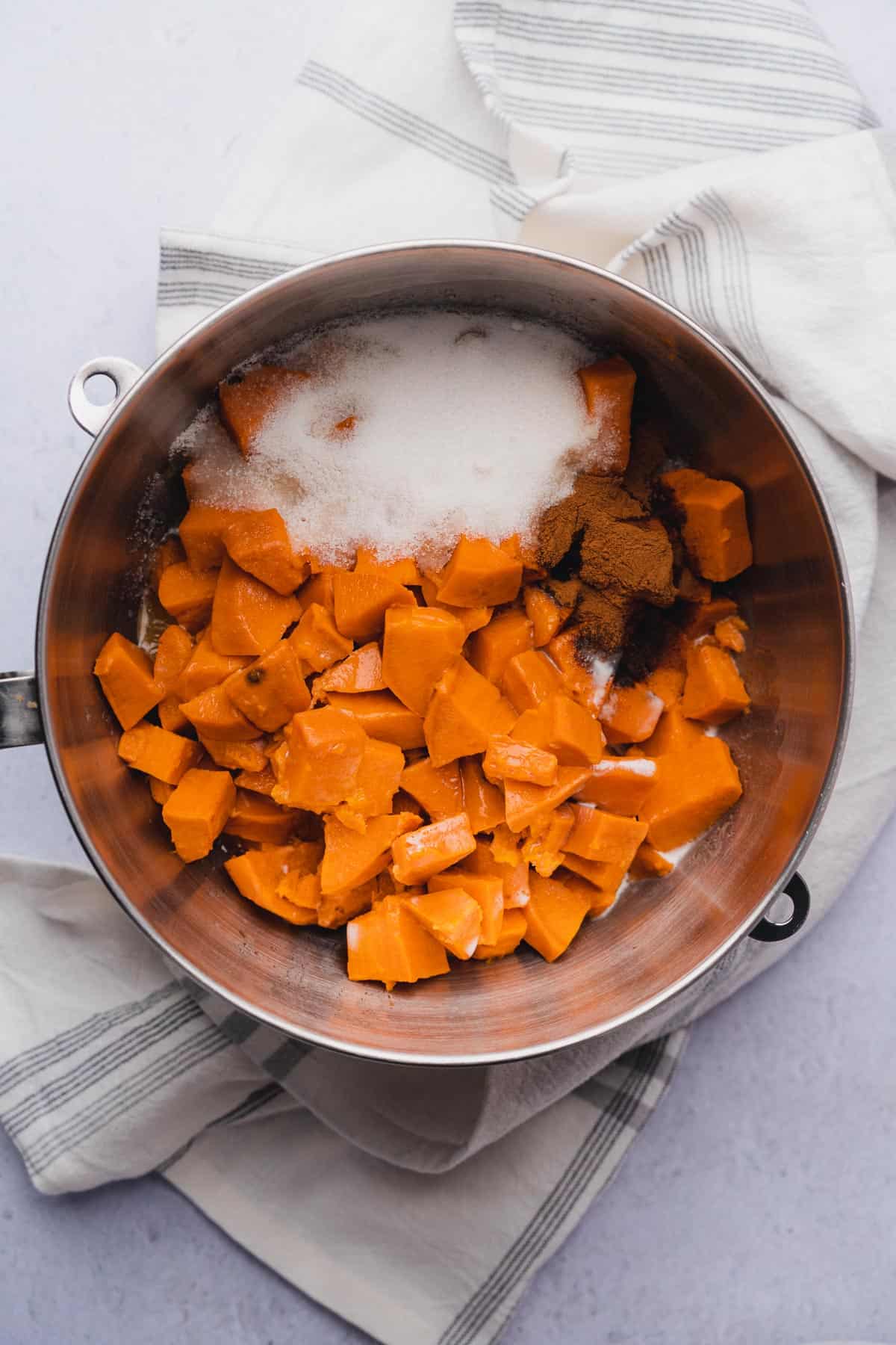 mashed sweet potatoes in a mixing bowl with sweetener, heavy cream, cinnamon, vanilla extract and melted butter