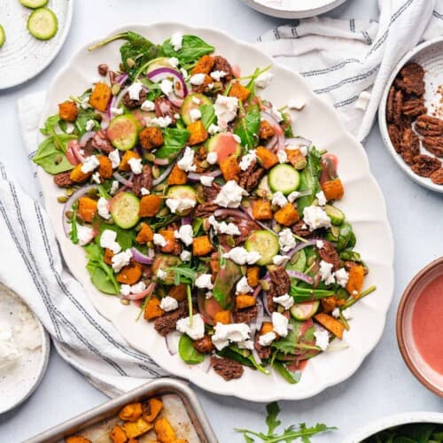 beautiful harvest salad recipe on a platter with cranberry dressing, candied pecans, butternut squash, goat cheese, cucumber slices, pepitas, red onions