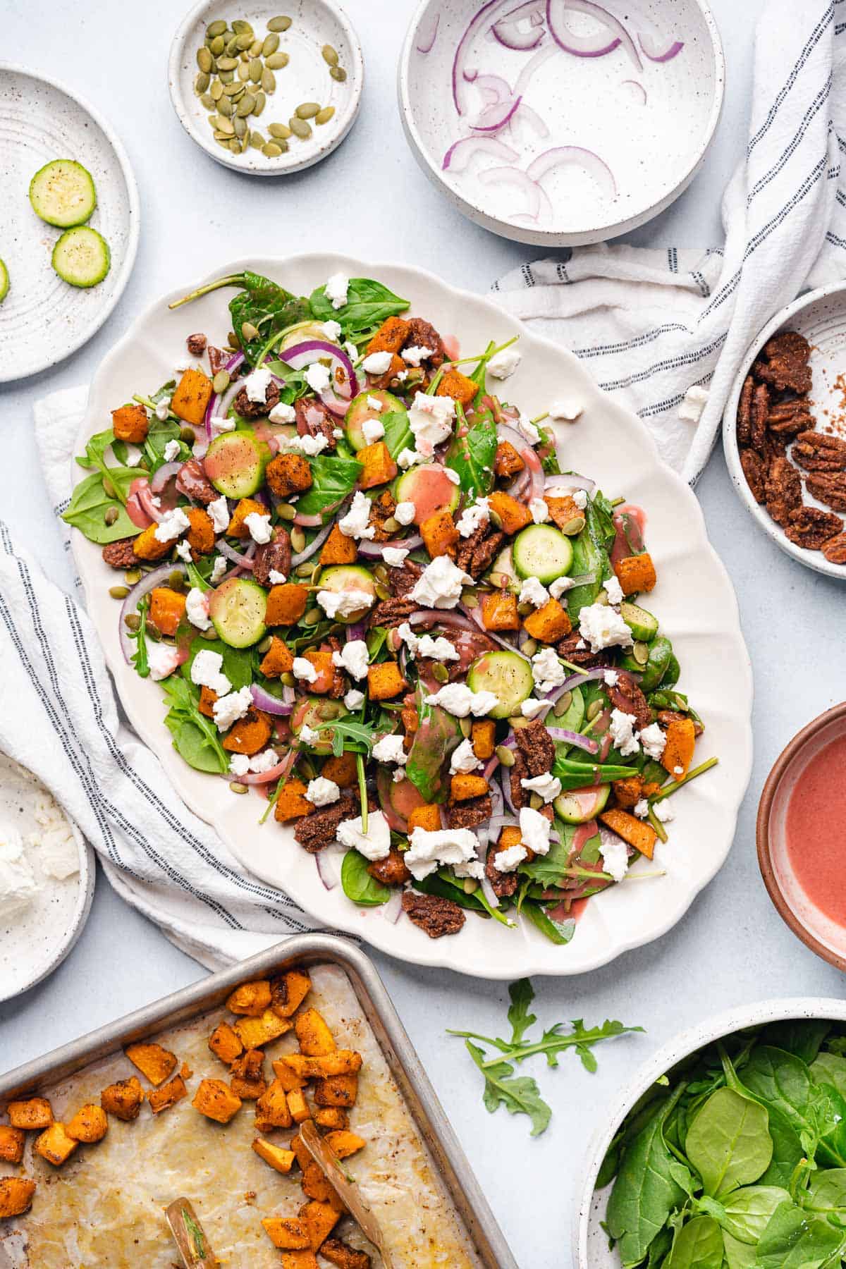 beautiful harvest salad recipe on a platter with cranberry dressing, candied pecans, butternut squash, goat cheese, cucumber slices, pepitas, red onions 