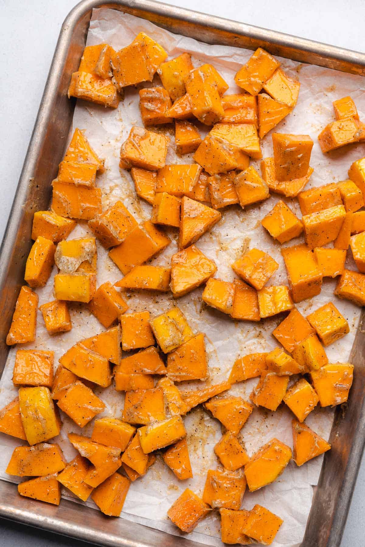 butternut squash coated with butter and seasonings on a parchment lined baking sheet