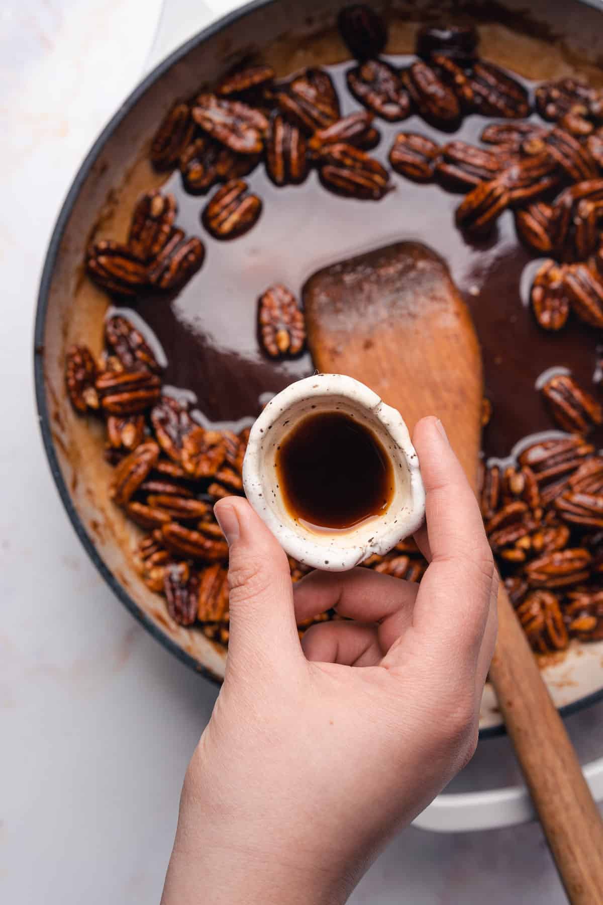 adding vanilla extract to a sweet buttery sauce with pecans