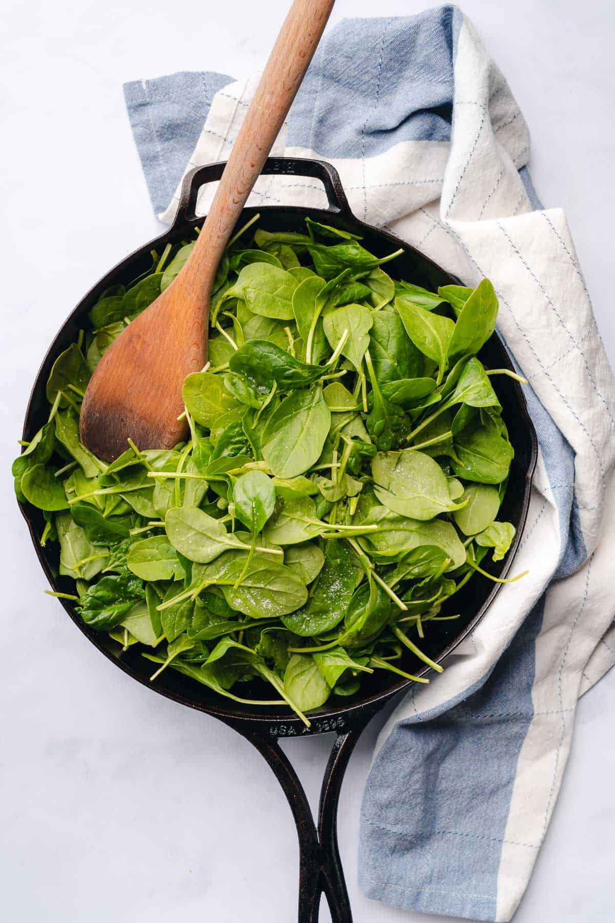 fresh spinach in a cast iron skillet with a wooden spoon