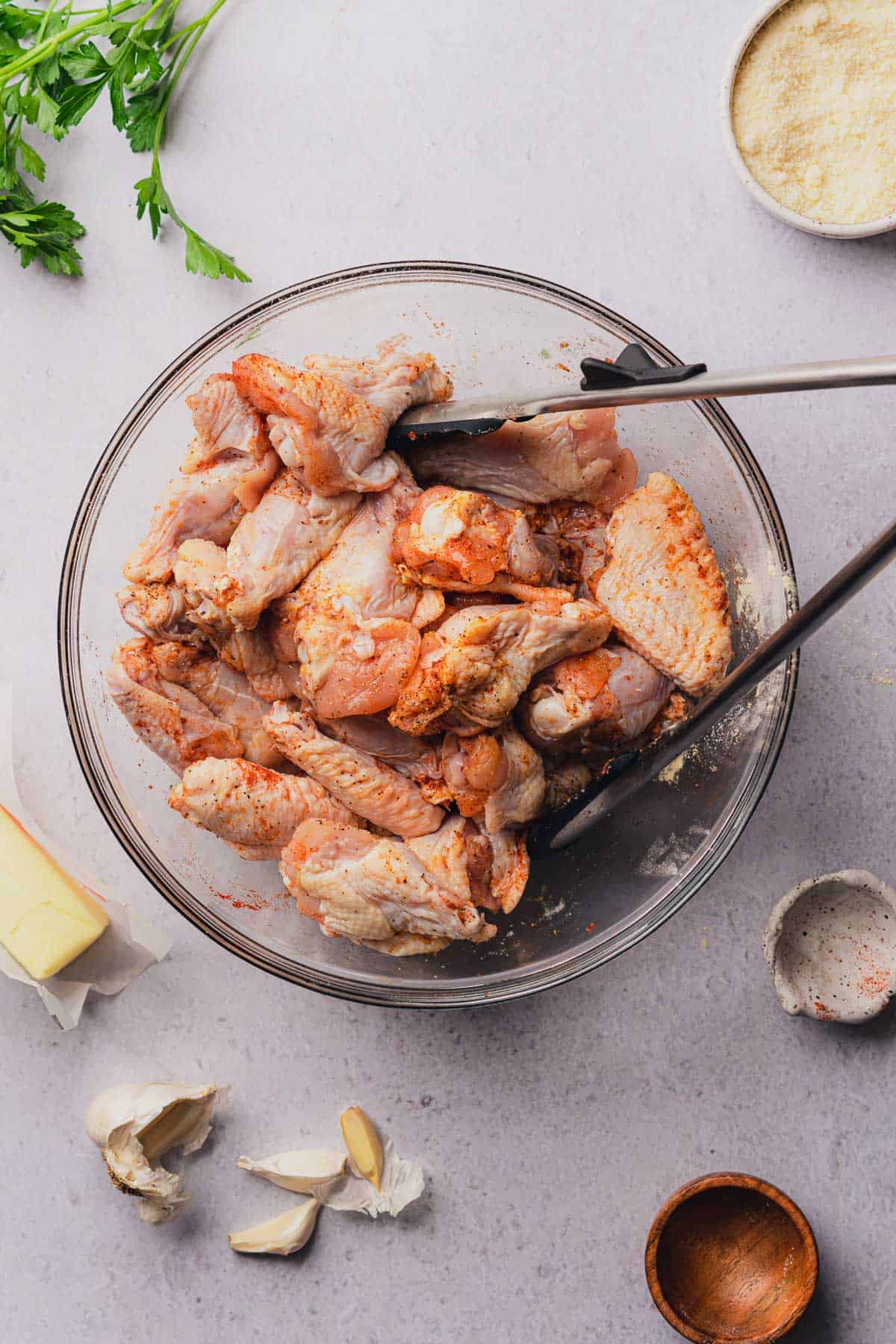tongs in a bowl of raw chicken wings to coat with seasonings and toss the mixture