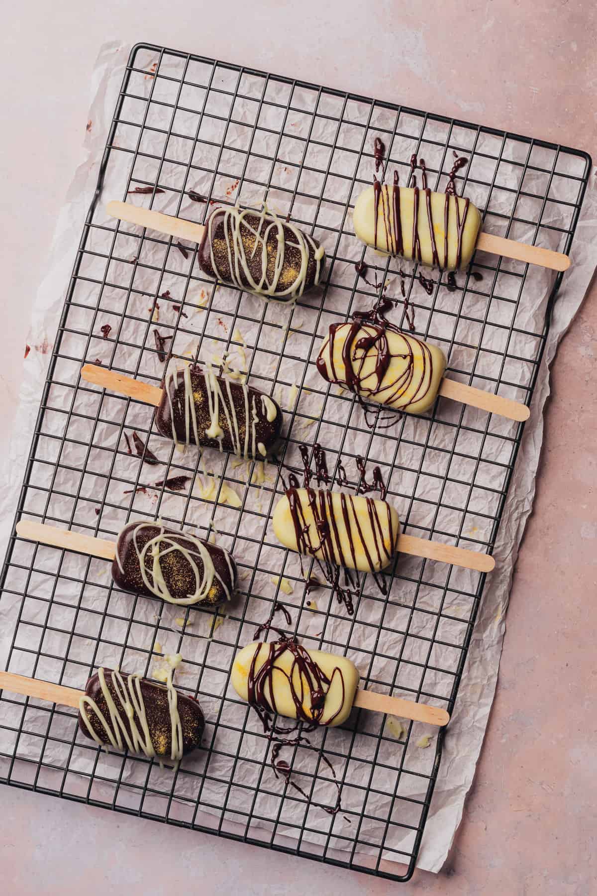 chocolate drizzle on top of  cakesicles on a cooling rack to catch chocolate drips