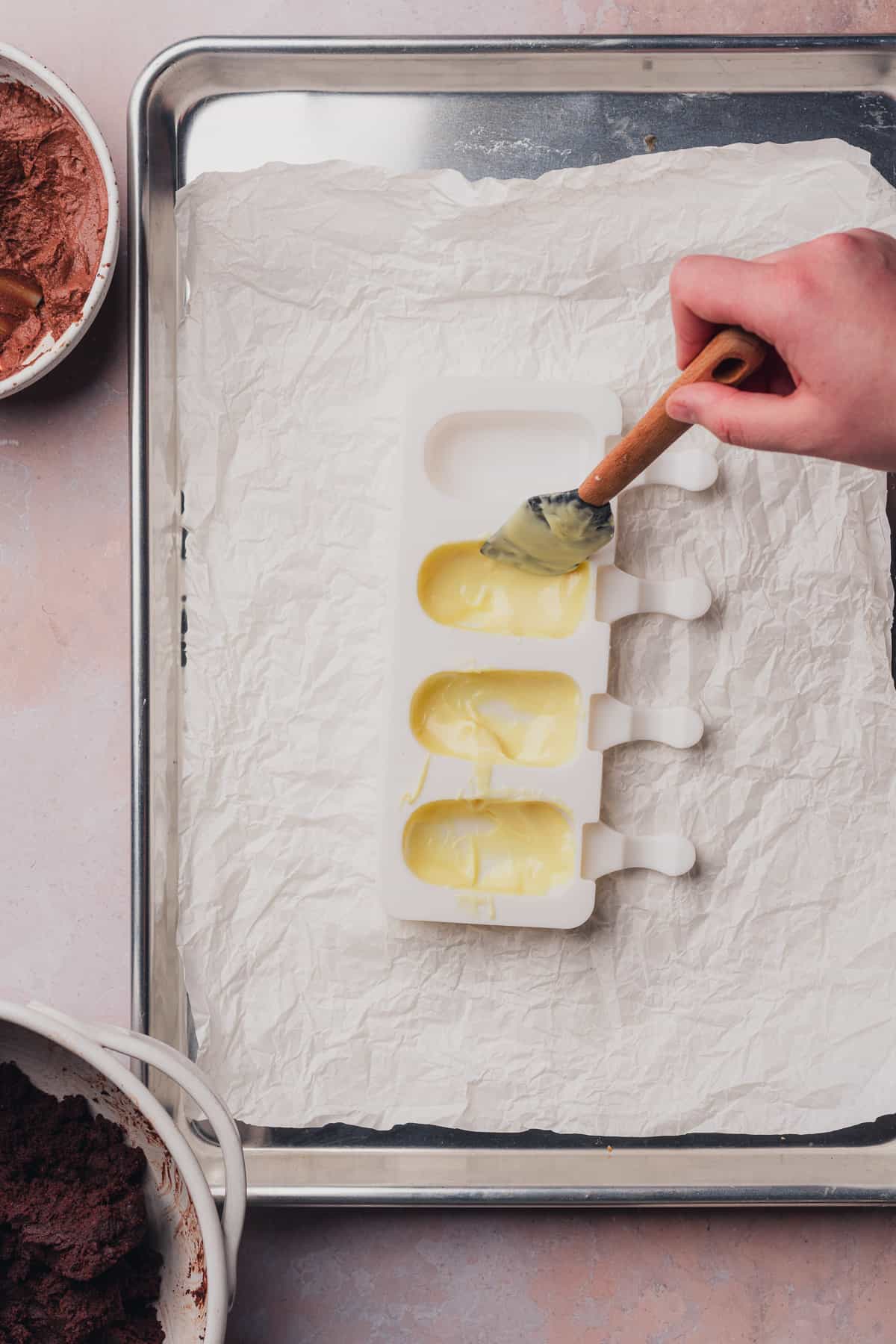 hand spreading white chocolate into a cakesicle mold with a rubber spatula
