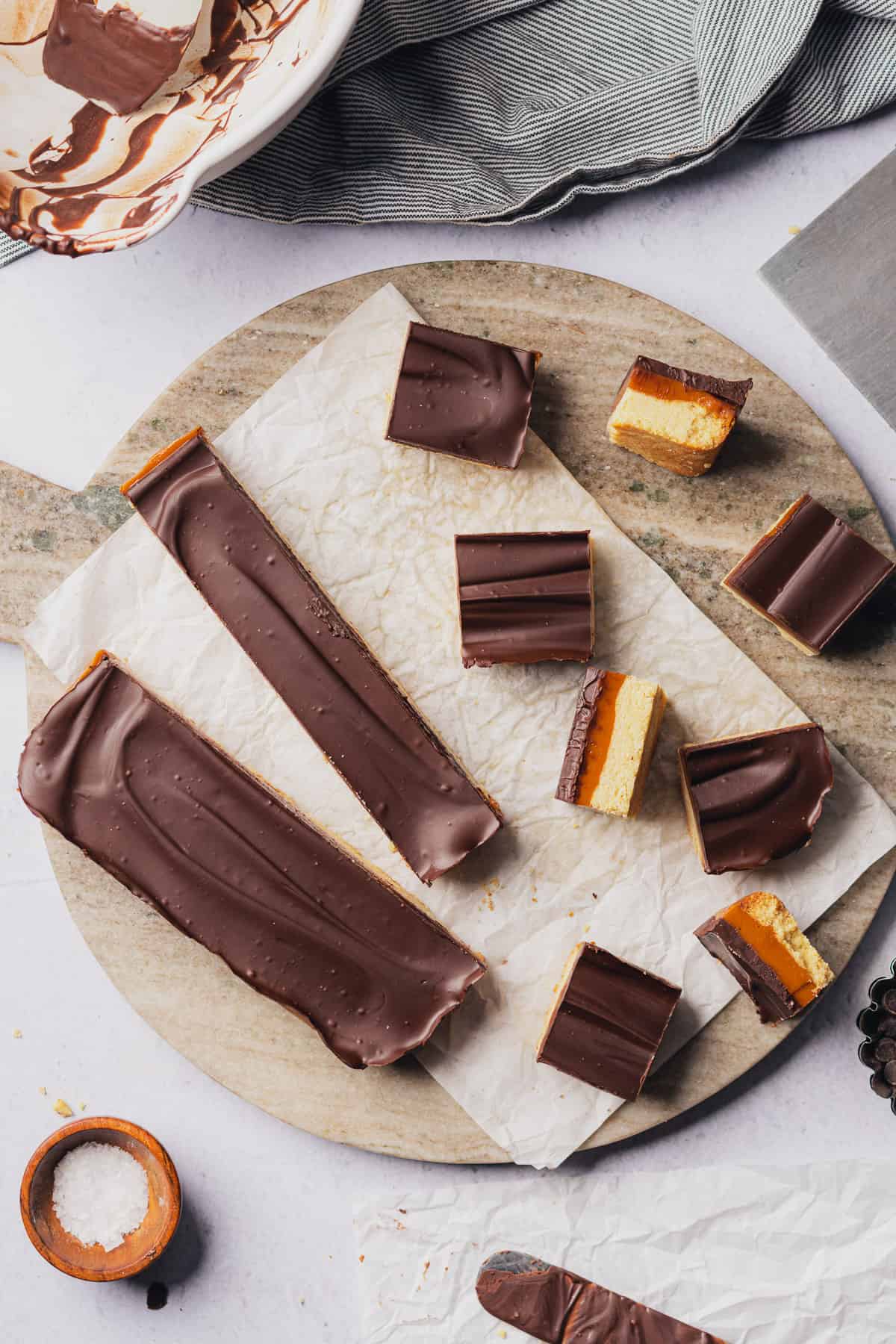 flatlay or keto caramel bars on a round marble surface with a piece of crinkled white parchment underneath, some flipped up to show the insides, and some laying flat 