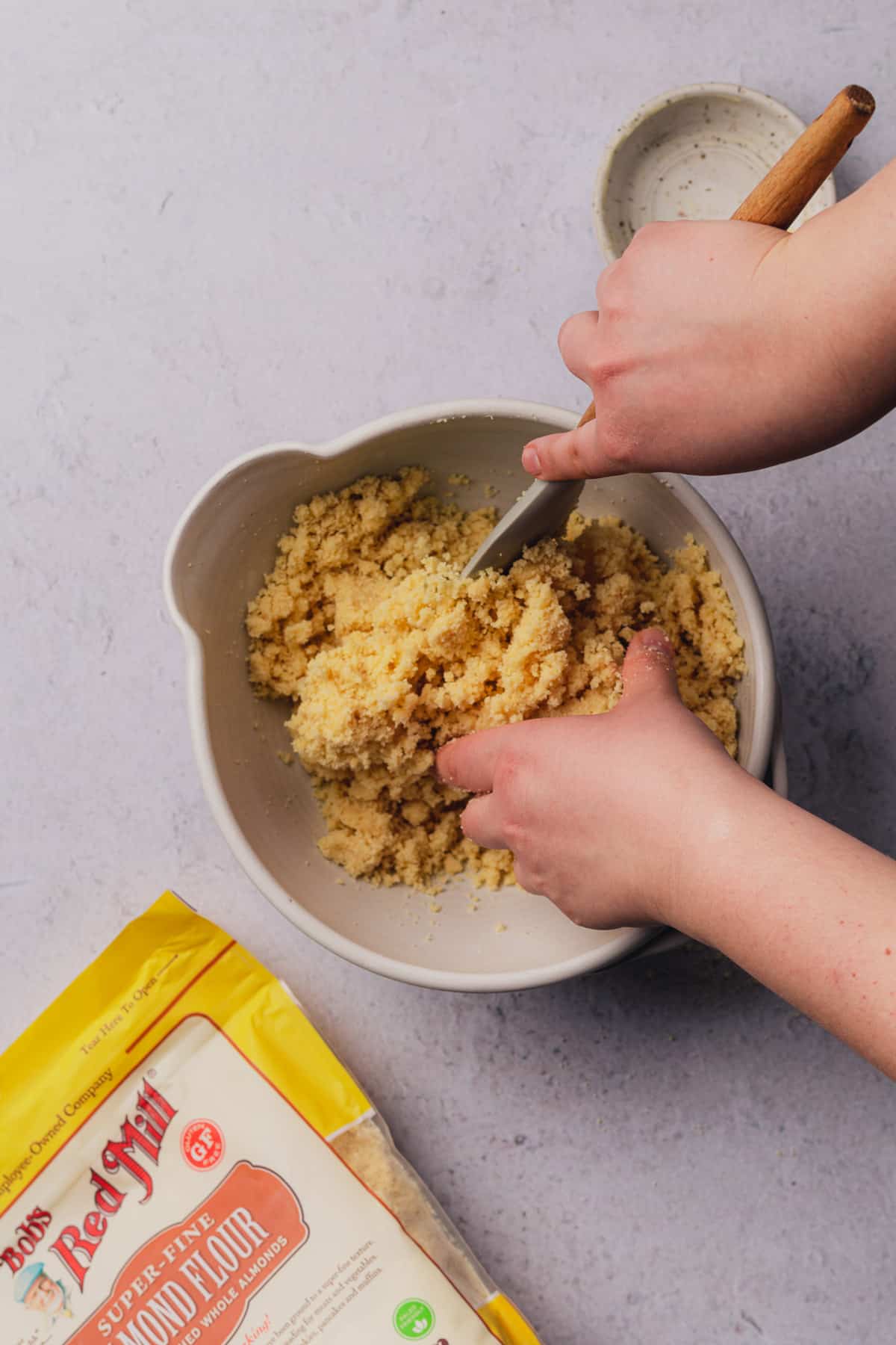 hands mixing together shortbread crust in a bowl with a rubber spatula