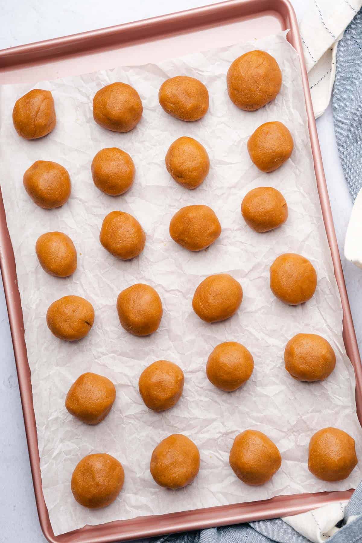 rolled peanut butter cookie dough balls on a parchment lined baking sheet