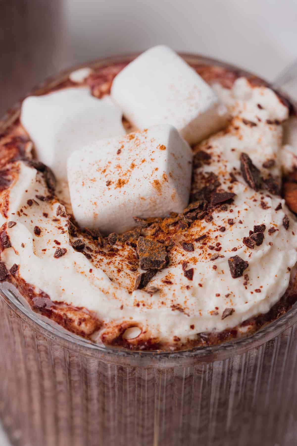 close up macro shot of instant pot hot chocolate with shaved chocolate, whipped cream and marshmallows in a glass mug