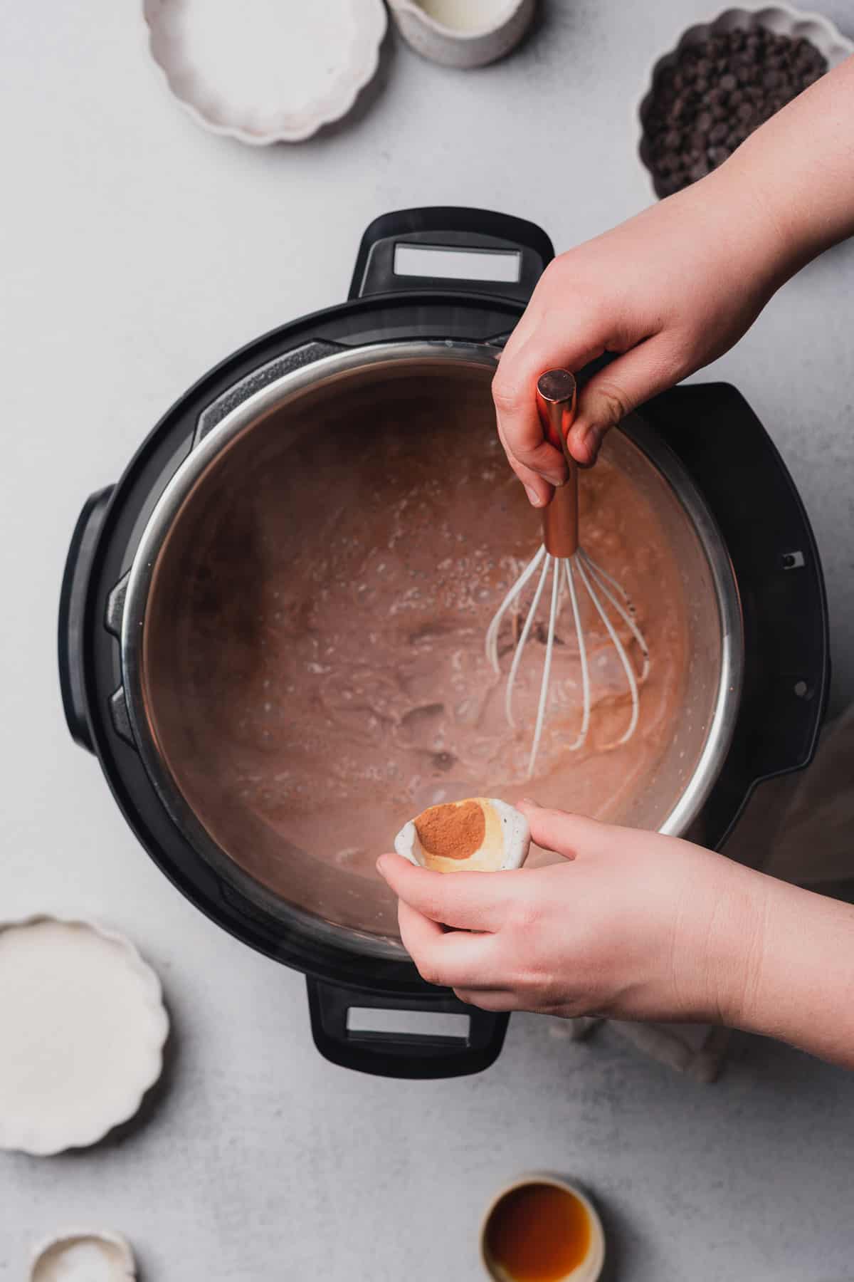 hand pouring cinnamon into instant pot while whisking hot chocolate 