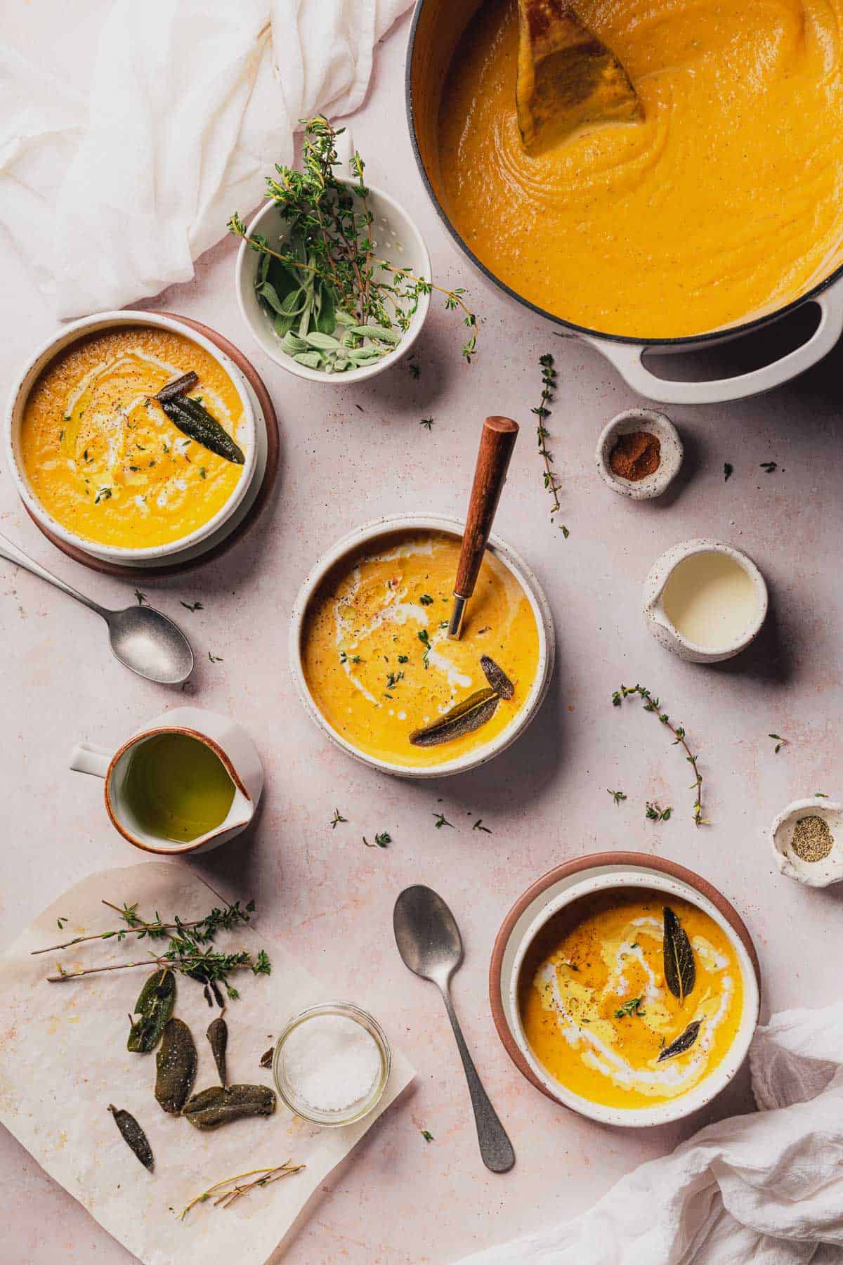 beautiful flat lay of 3 bowls of creamy keto butternut squash soup with fresh herbs, cream, and olive oil