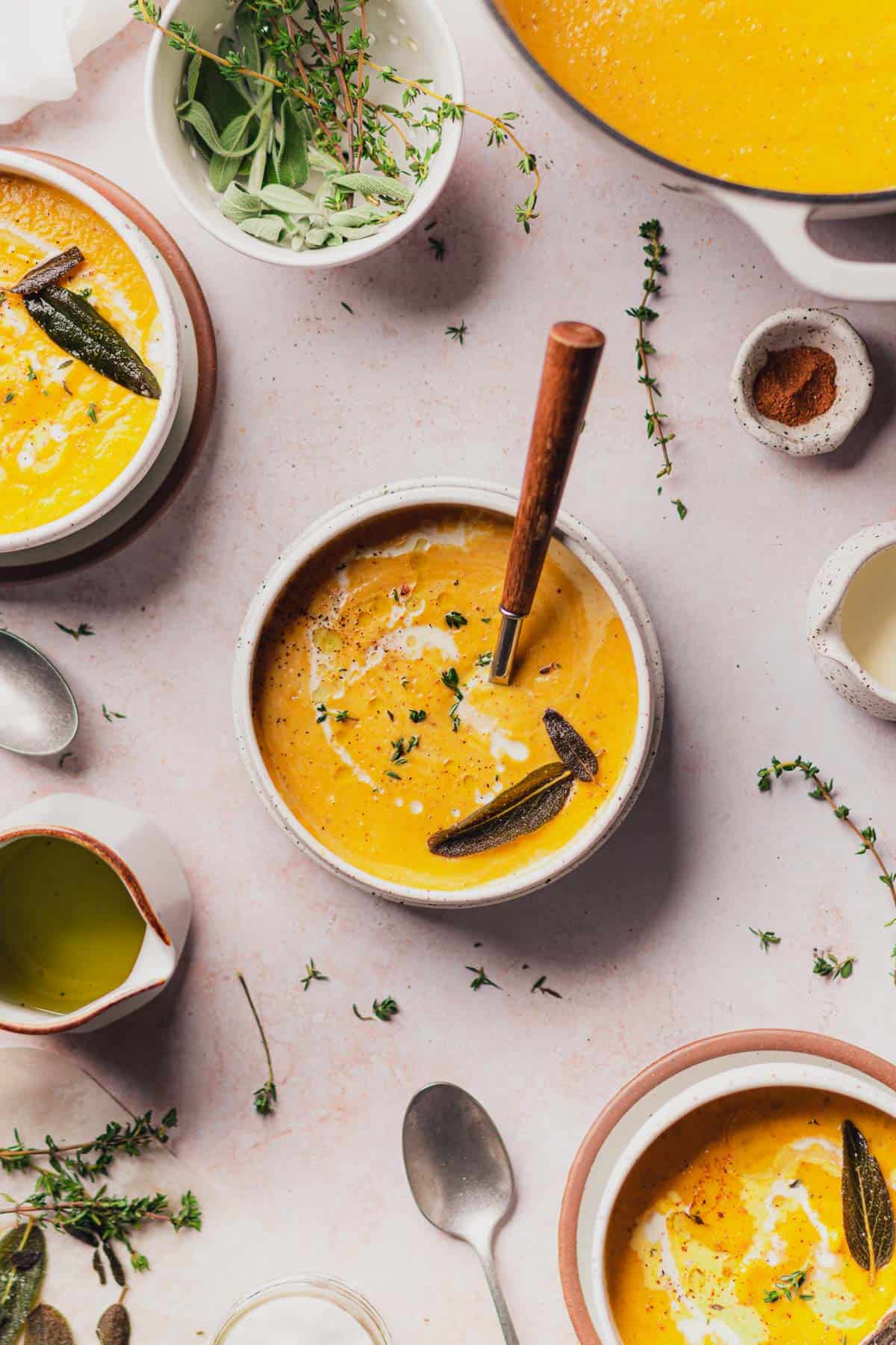 3 bowls of creamy butternut squash soup with fried sage, fresh thyme, nutmeg, olive oil and cream