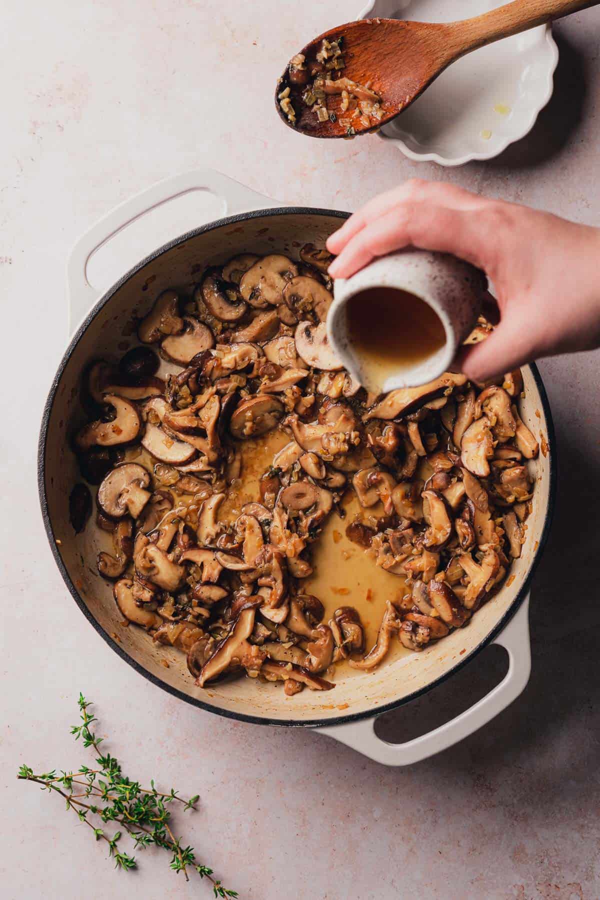 mushrooms in a skillet and a hand pouring in beef broth 