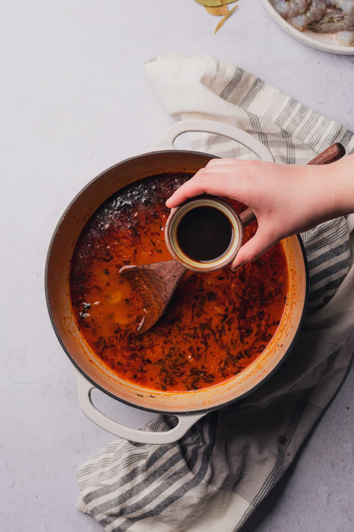 hand holding Worcestershire sauce overtop of a dutch oven 