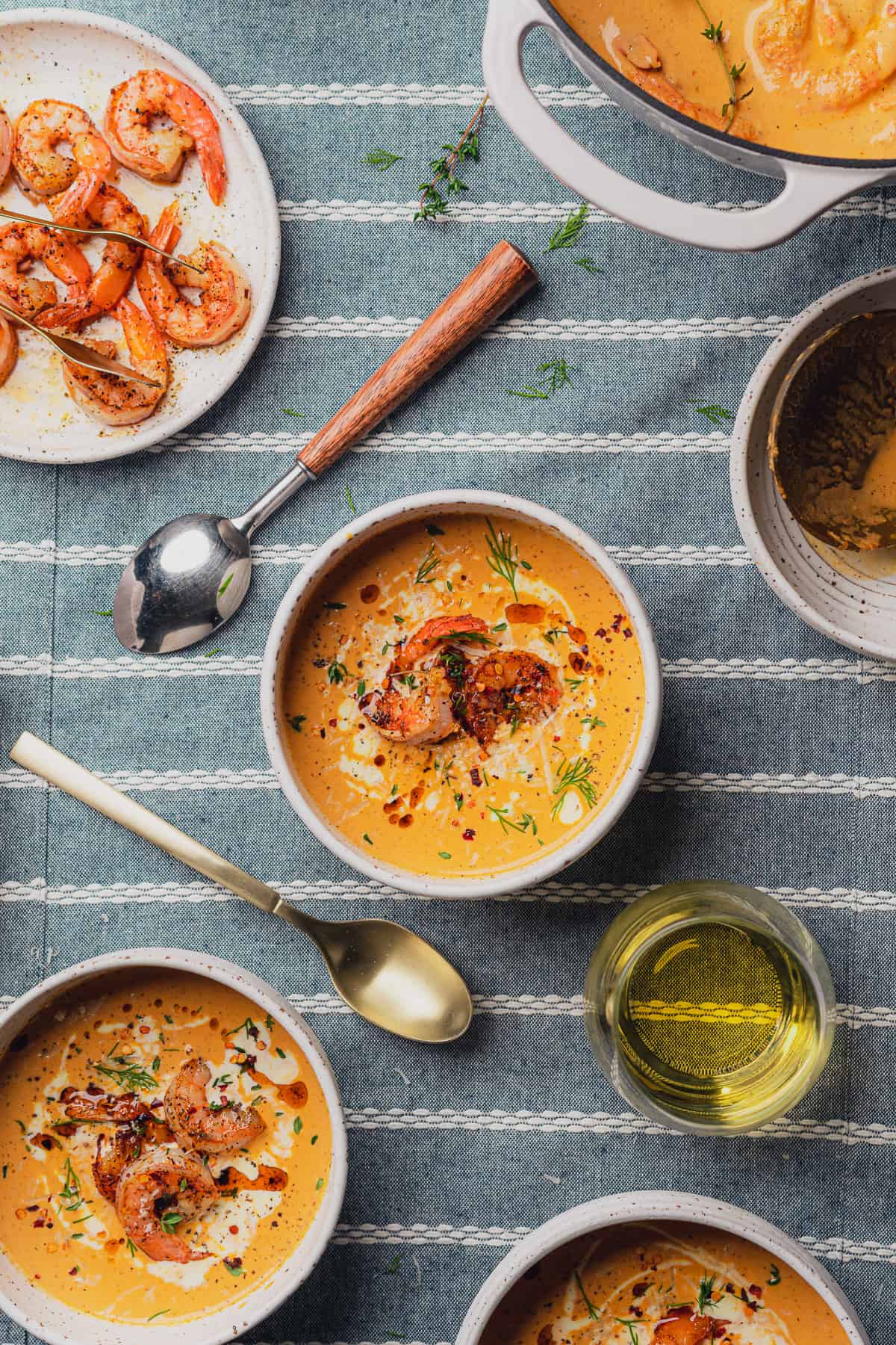 flat lay shot of two bowls of keto shrimp bisque with a glass of wine nearby and a plate of freshly cooked shrimp 