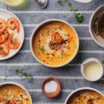 keto shrimp bisque on black back drop with 3 bowls of soup with herbs, shrimp, cream and white wine