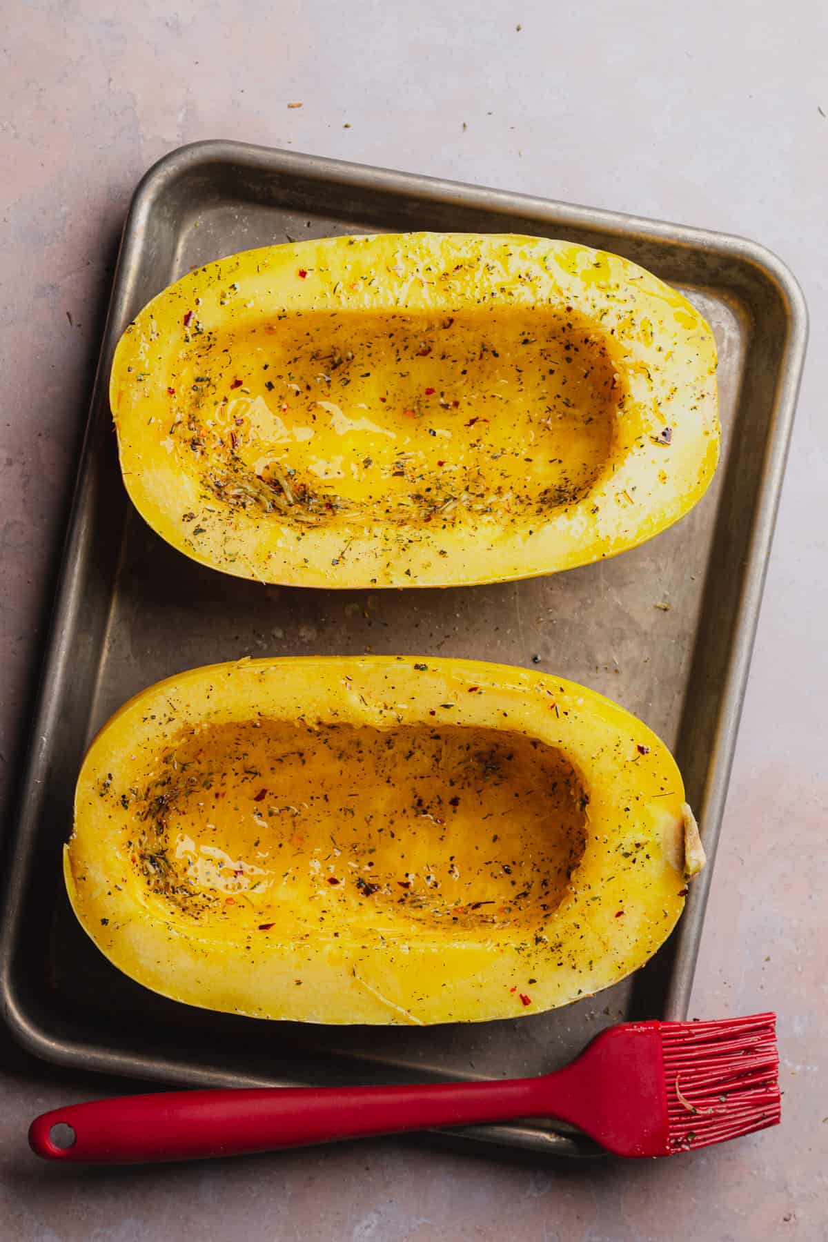 spaghetti squash cut in half with olive oil, salt, and pepper on a baking sheet 