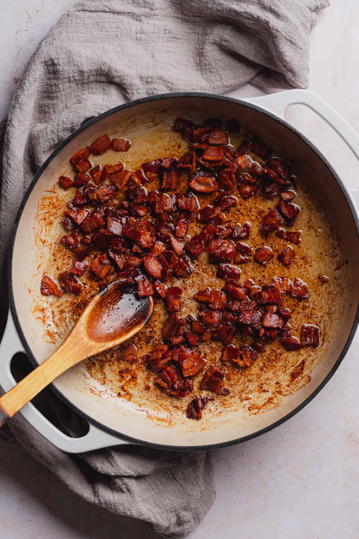 cooking bacon in an enameled dutch oven with a wooden spoon