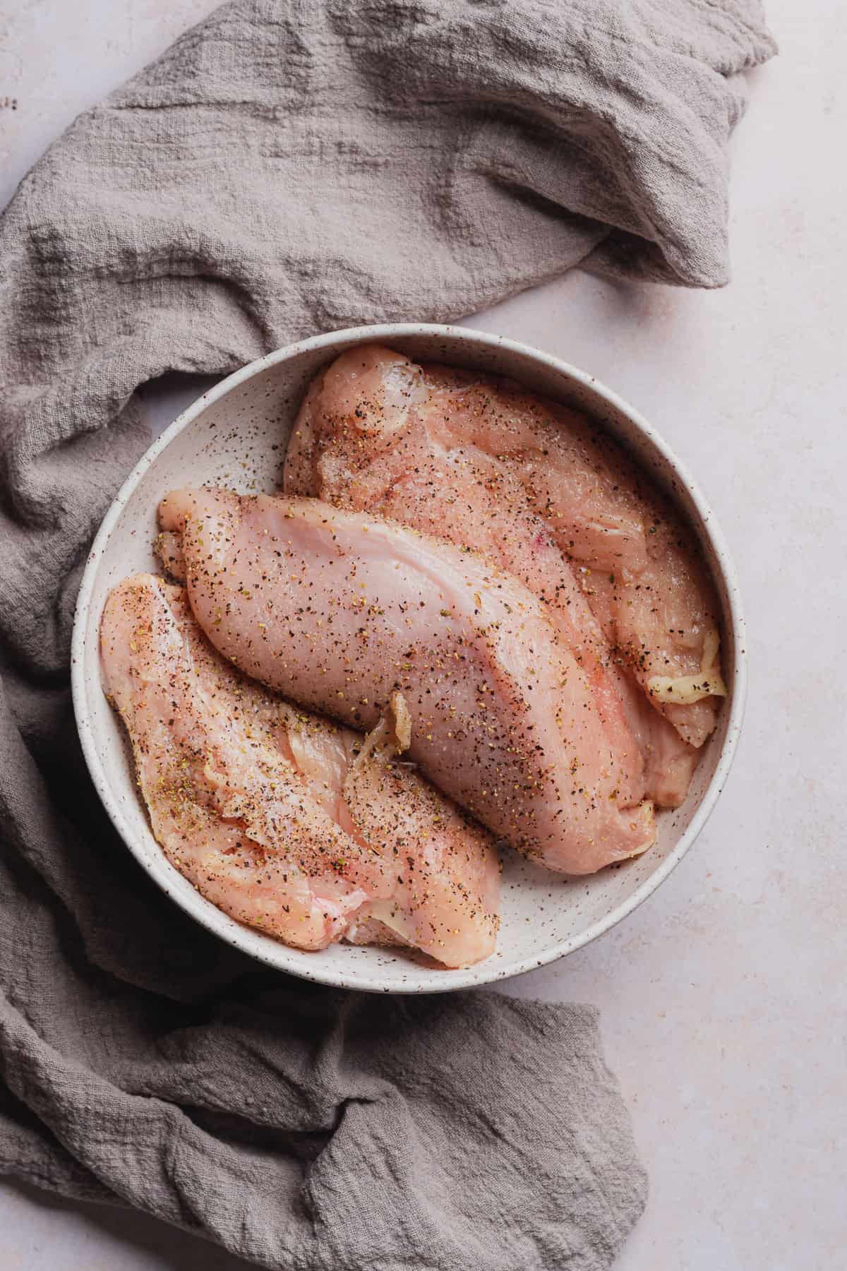 raw seasoned chicken breasts in a ceramic bowl