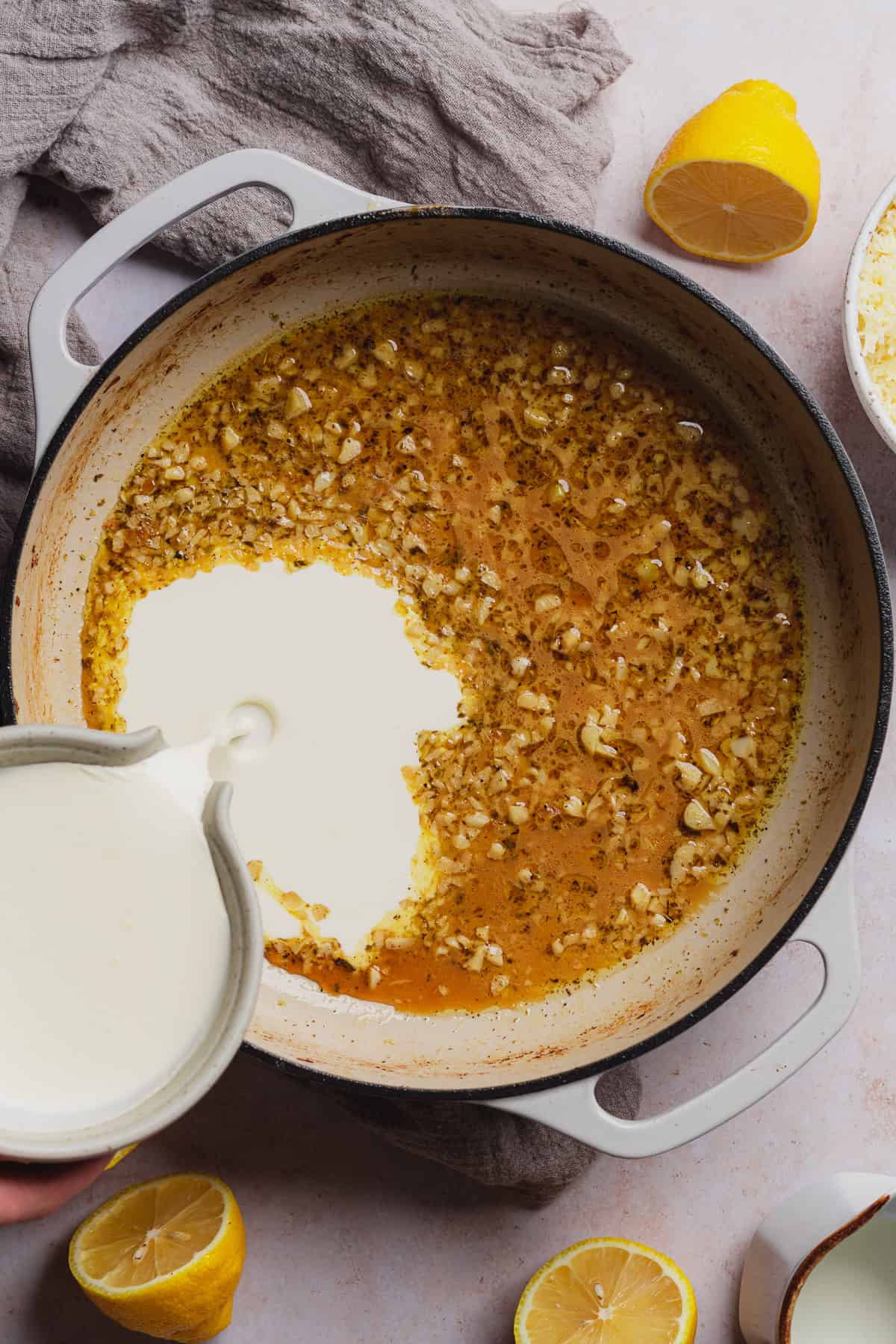 pouring heavy cream into an enameled cast iron with white wine pan sauce