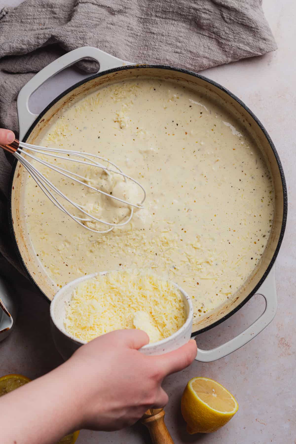 pouring freshly shredded parmesan cheese into a creamy sauce with a whisk mixing everything together
