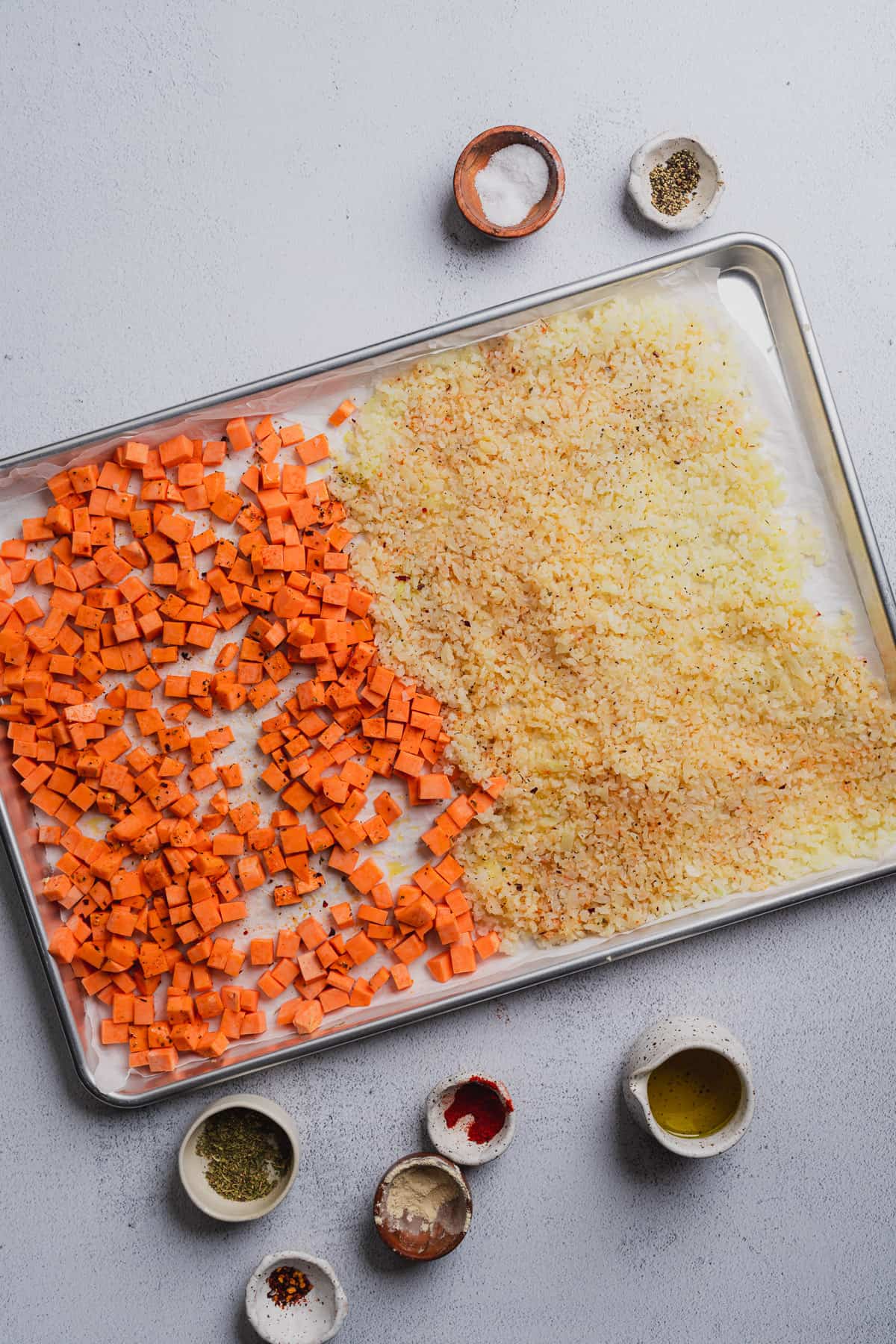 raw riced cauliflower and sweet potato cubes on a large baking sheet with parchment paper 