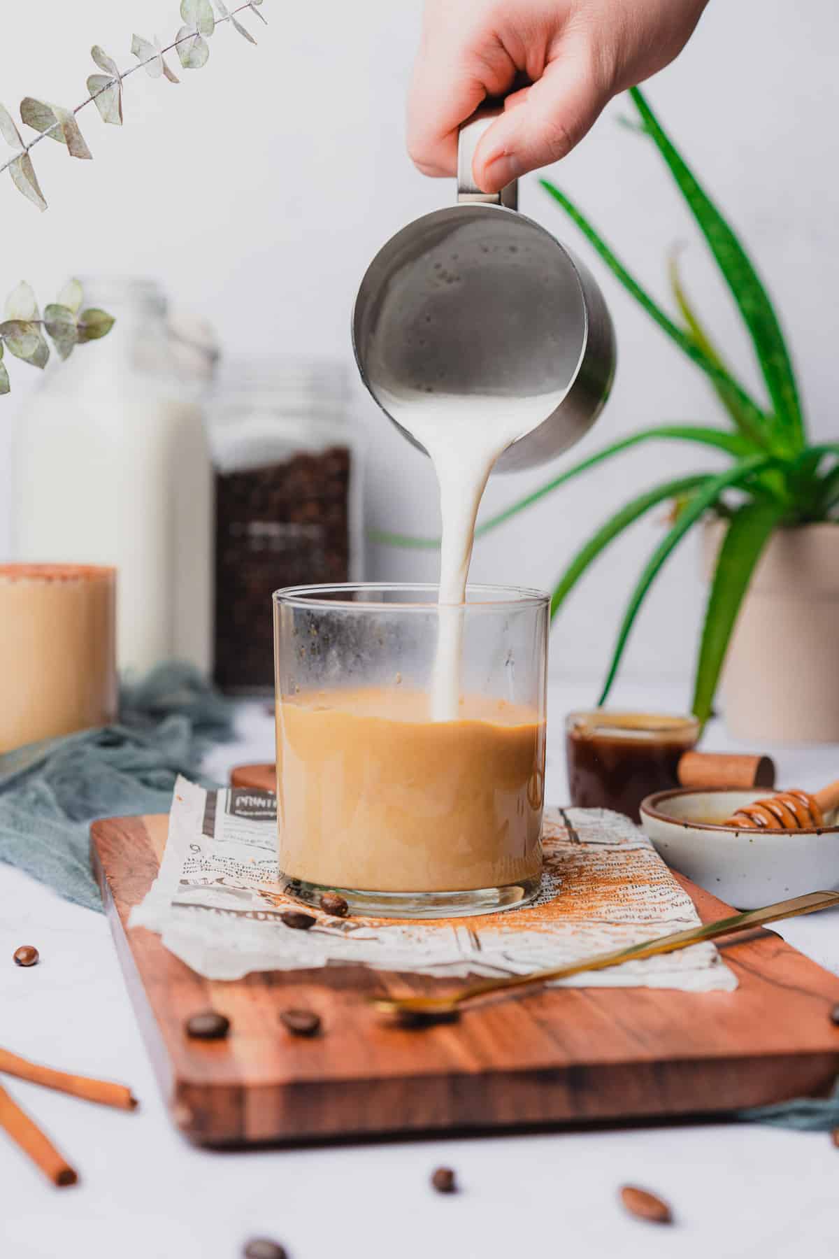 pitcher pouring in steamed milk to a glass of coffee