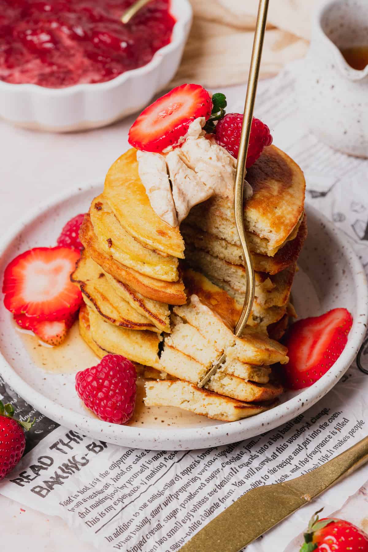 stack of fluffy keto coconut flour pancakes with a large bite being taken out with a fork, topped with butter and strawberries 
