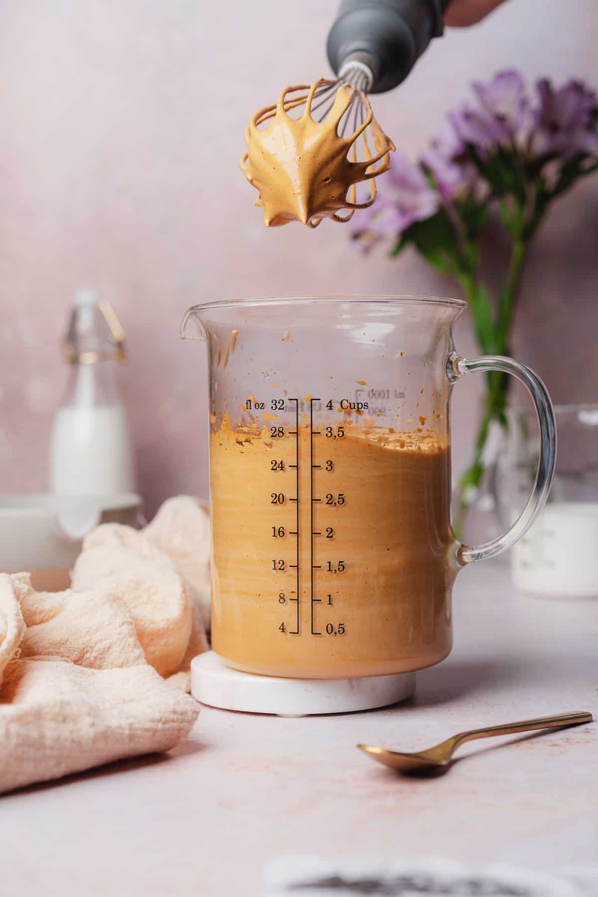 keto whipped coffee foam with a whisk held above the beaker to show the texture 
