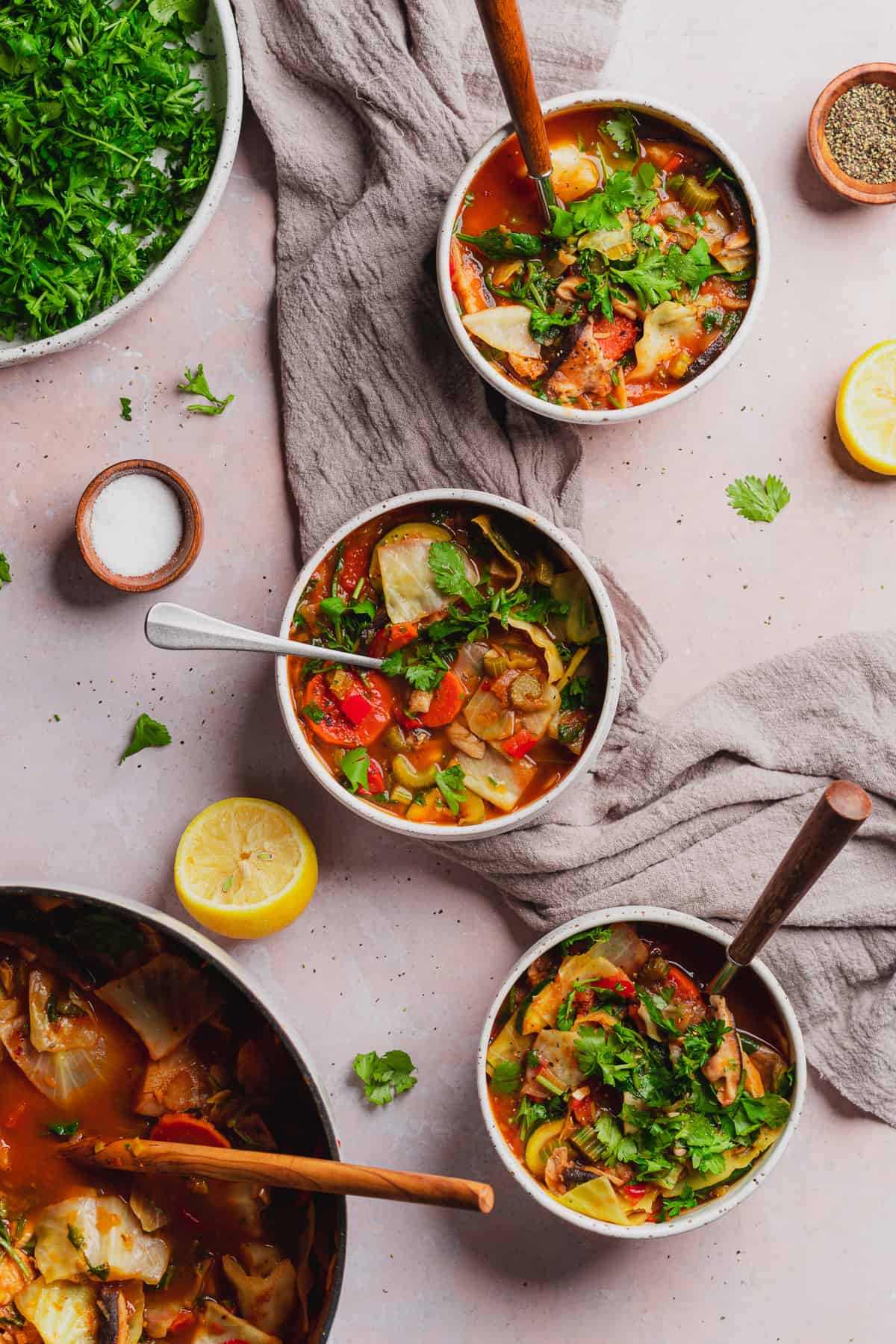 keto and vegan vegetable soup recipe in a bowl surrounded by lemons, fresh herbs, salt and pepper