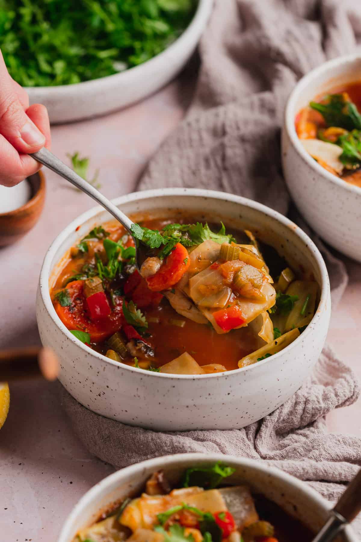 keto vegan vegetable soup with a hand on a spoon and lifting it from the bowl