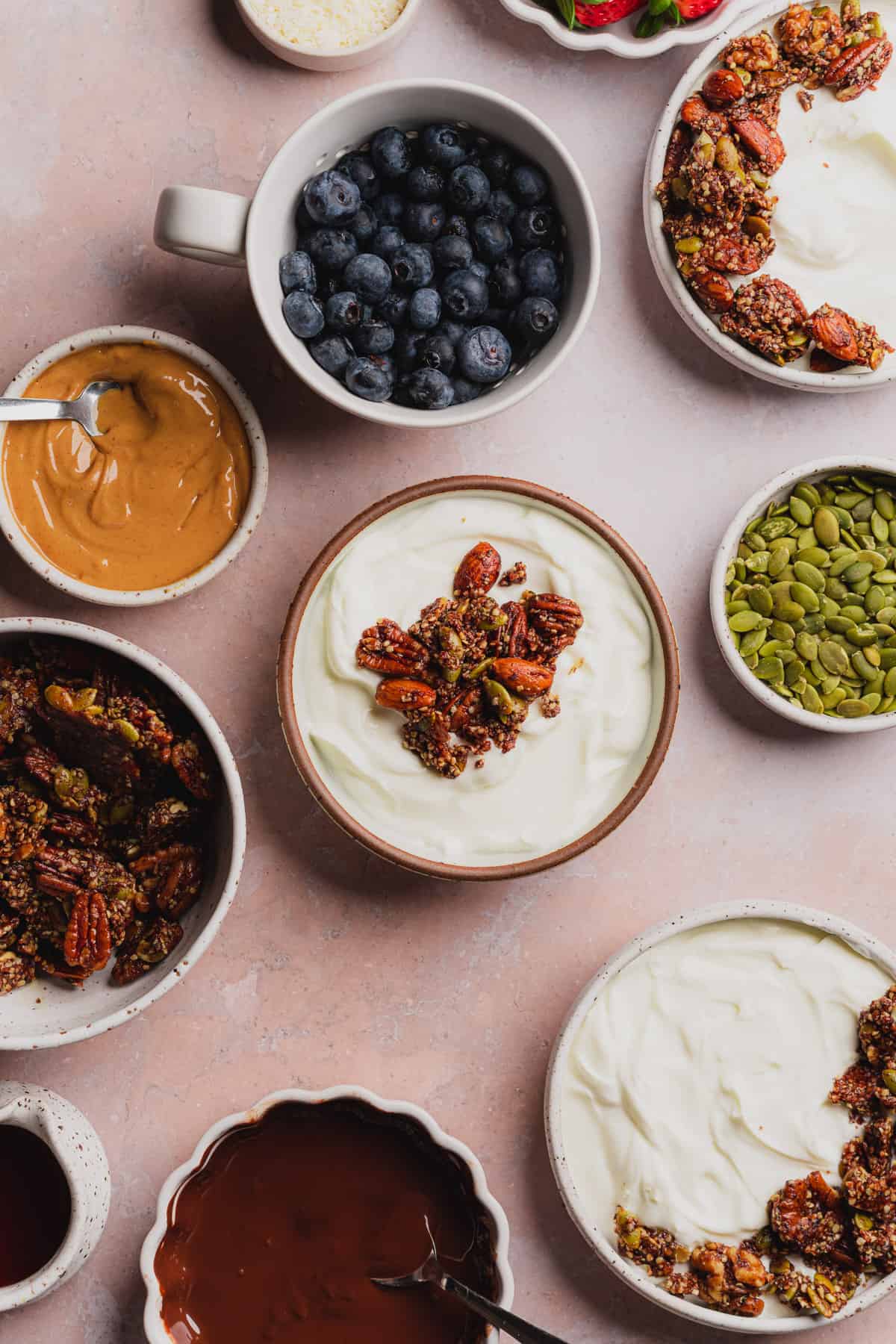 greek yogurt topped with granola, surrounded by fruit, pepitas, and other toppings. 