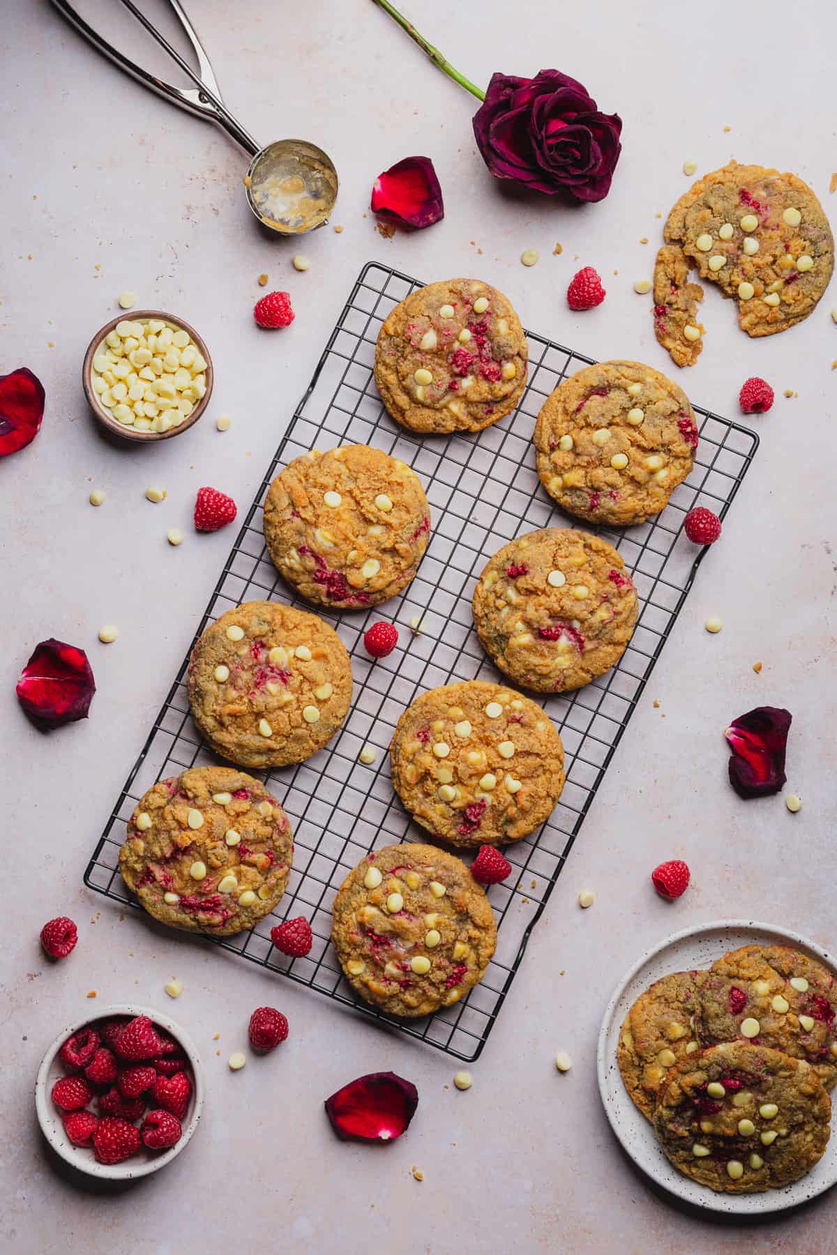 raspberry white chocolate cookies on a cooling rack surrounded by rose petals and fresh raspberries