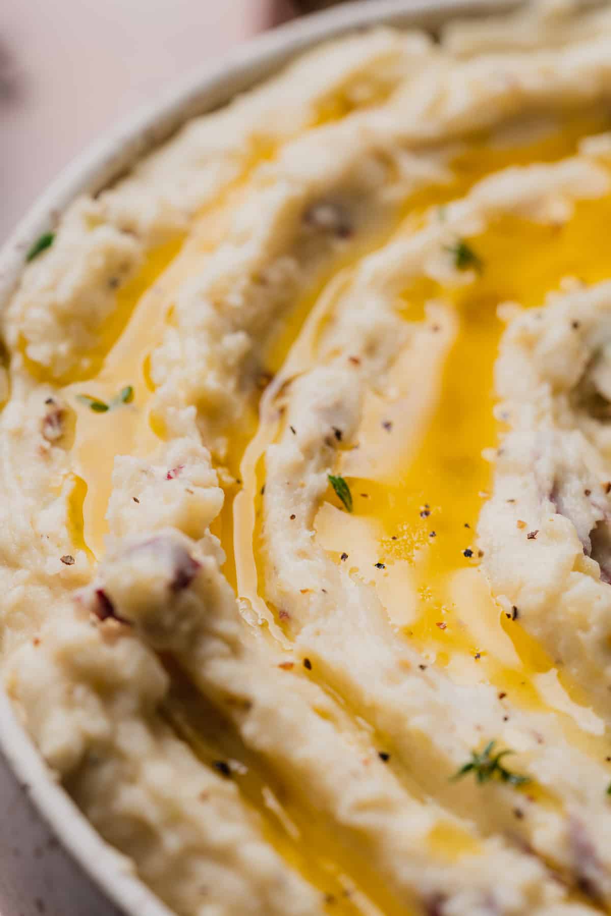 macro shot showing up close of a redskin mashed potatoes with small chunks, melted butter and fresh thyme 