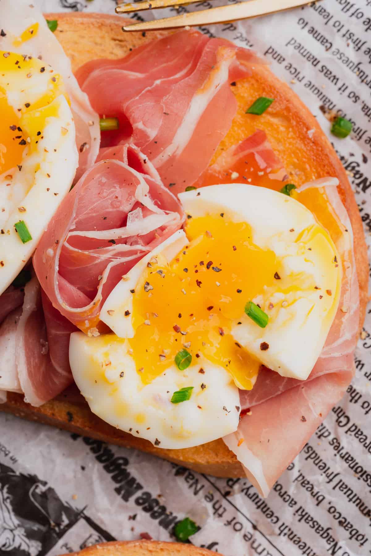 very close up shot of a smashed egg on prosciutto toast with chives 