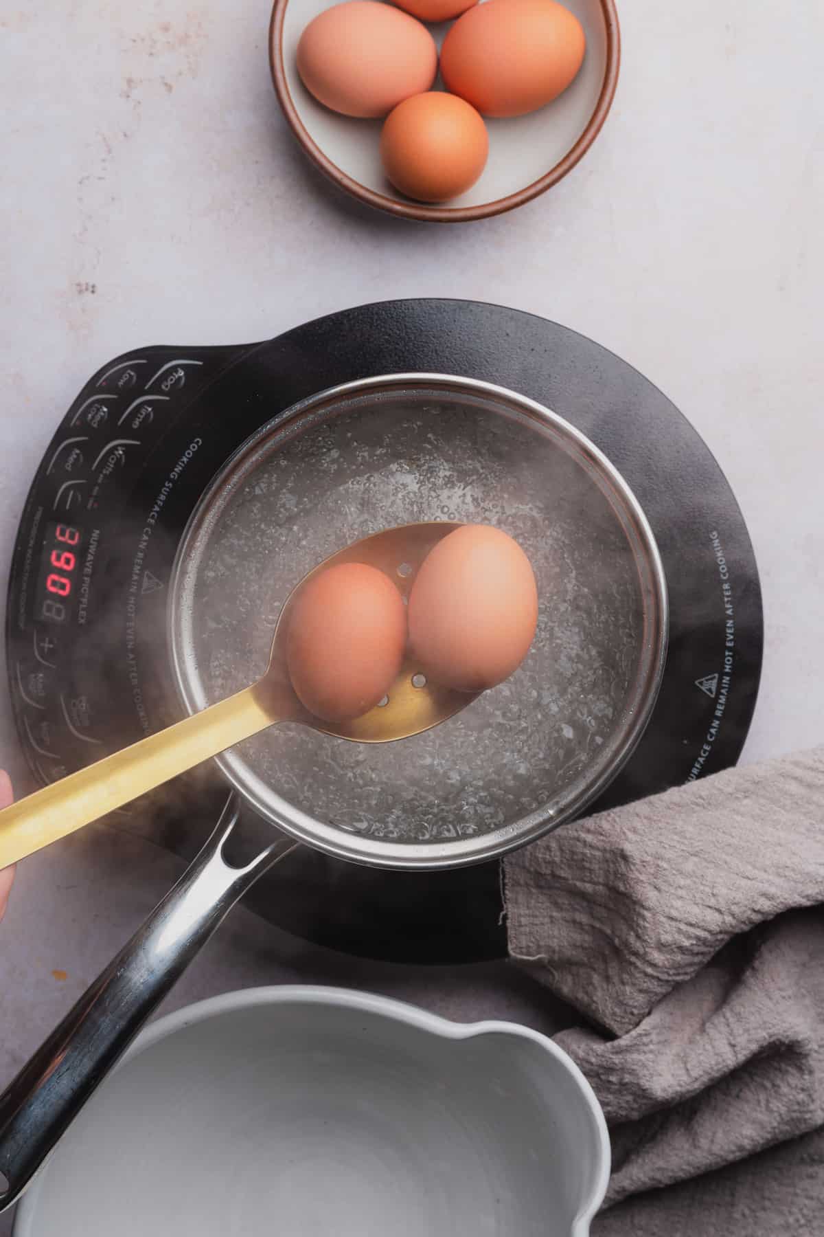large slotted spoon holding eggs going into boiling water