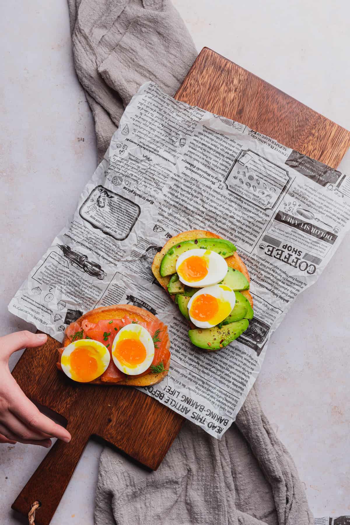 hand placing egg toast on newspaper on top of a dark brown cutting board 