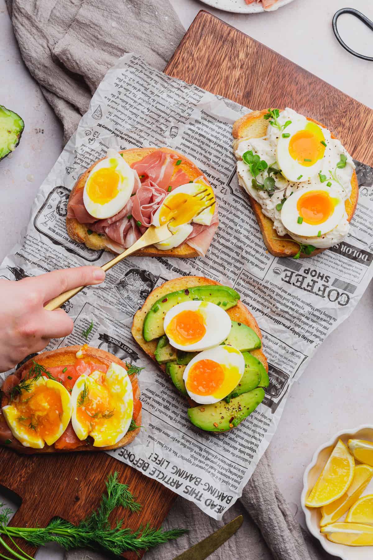 hand using a fork to smash yolky soft boiled eggs on top of toast with delicious toppings 