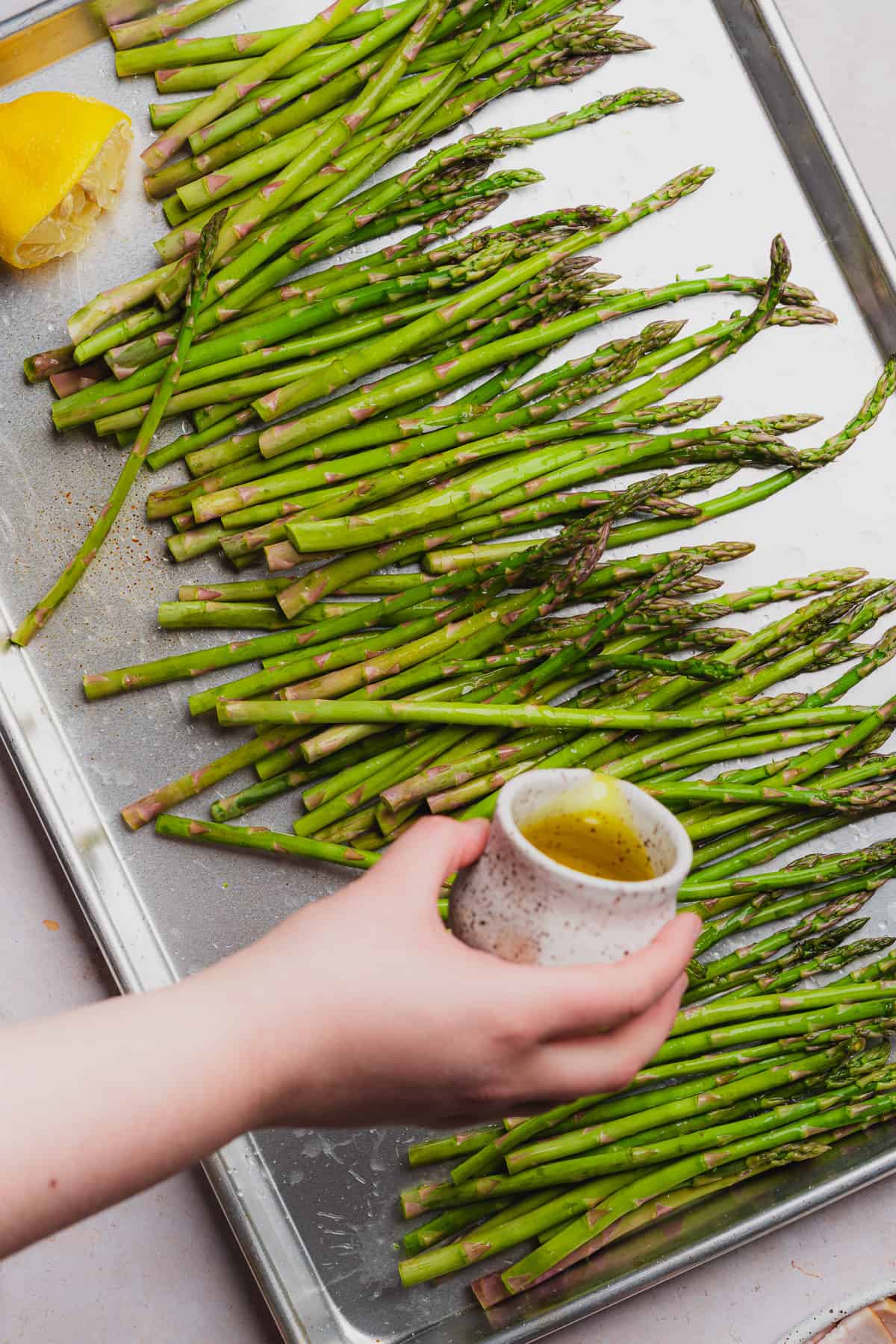 hand pouring olive oil over top of asparagus spears