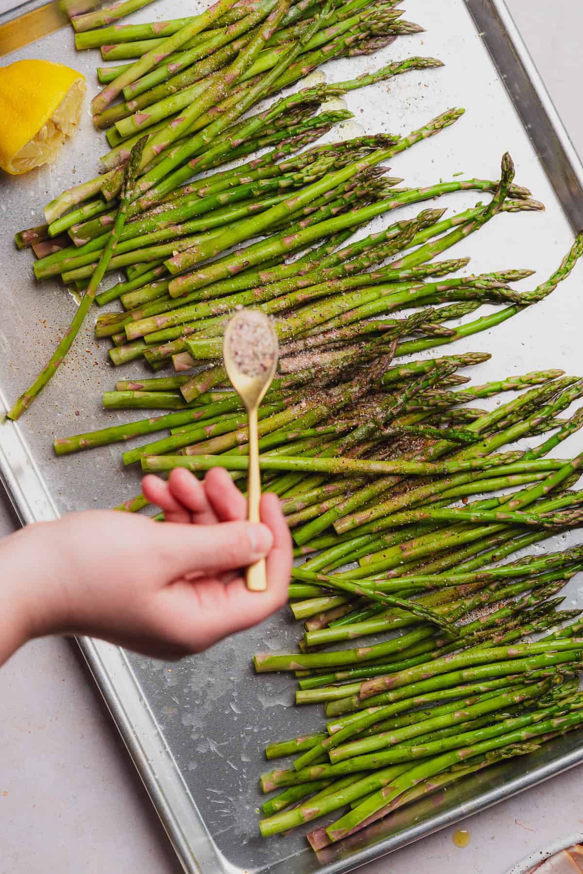 hand sprinkling seasoning over top of asparagus 