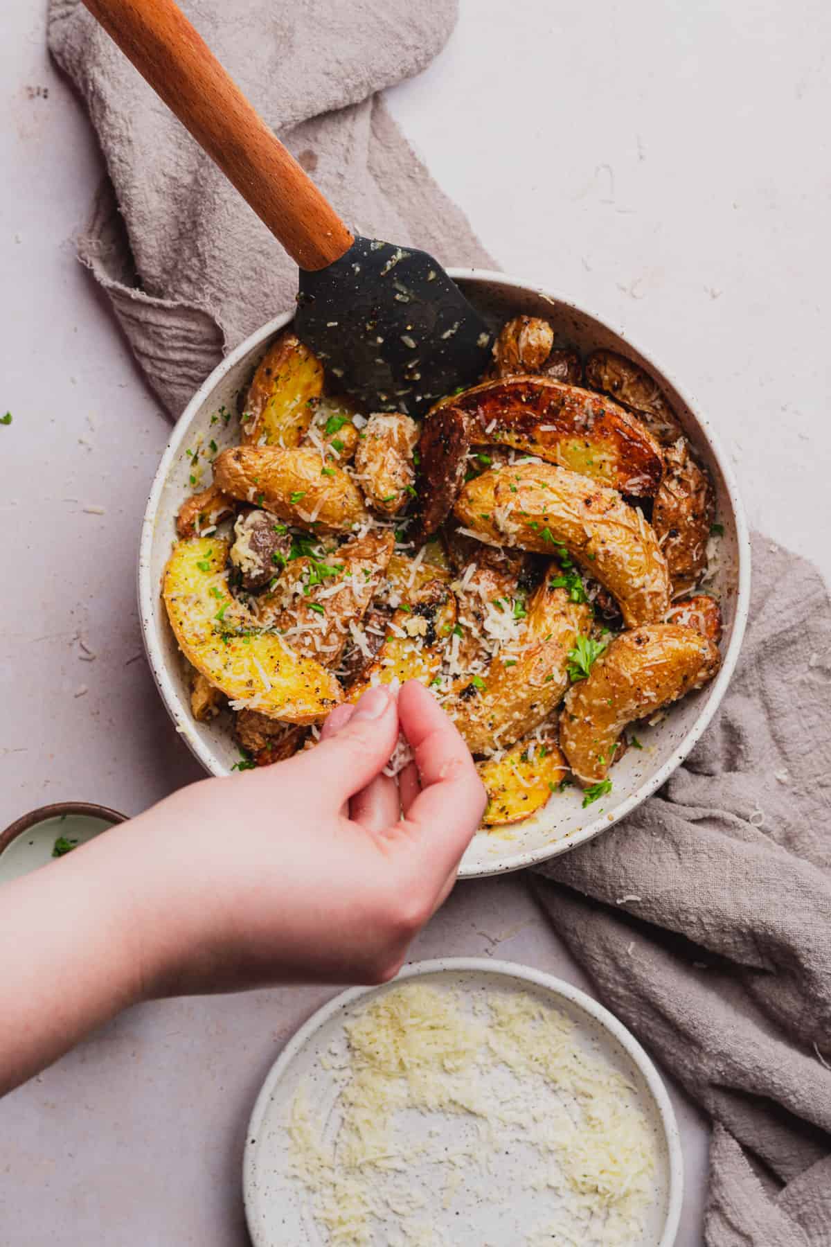 hand sprinkling parsley and cheese over top of fingerling potatoes 