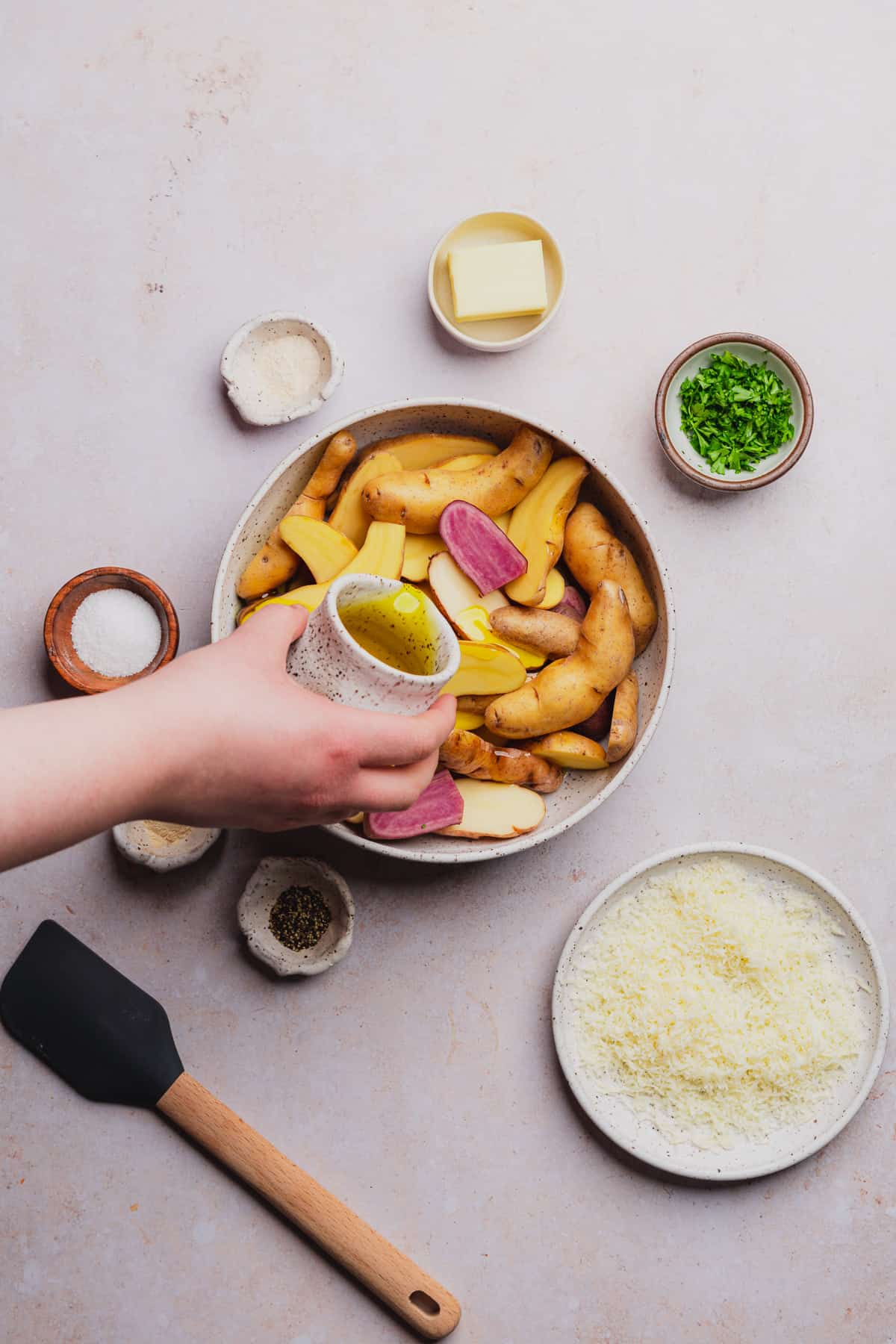 hand pouring olive oil onto fingerling potatoes in a bowl