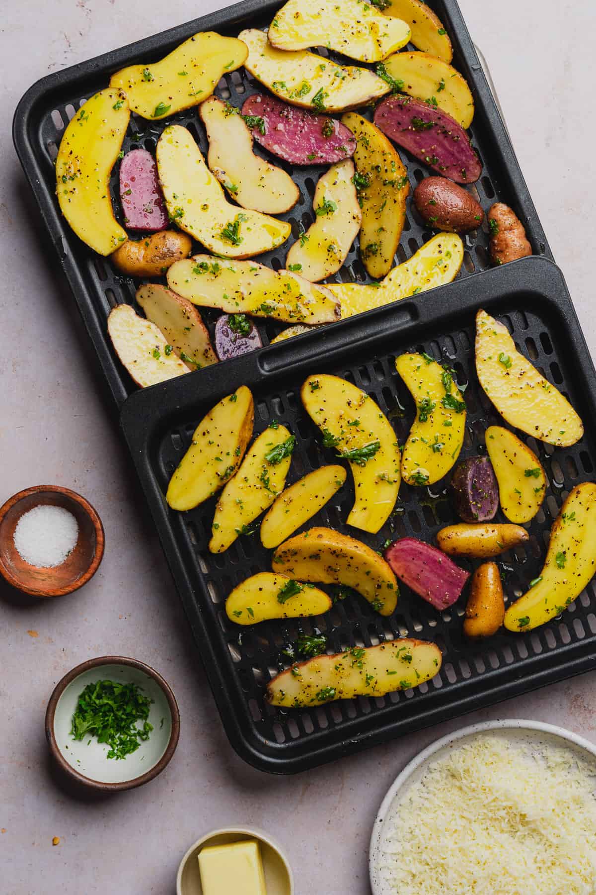 air fryer fingerling potatoes with parsley, salt, and pepper on air fryer trays getting ready to go into the air fryer
