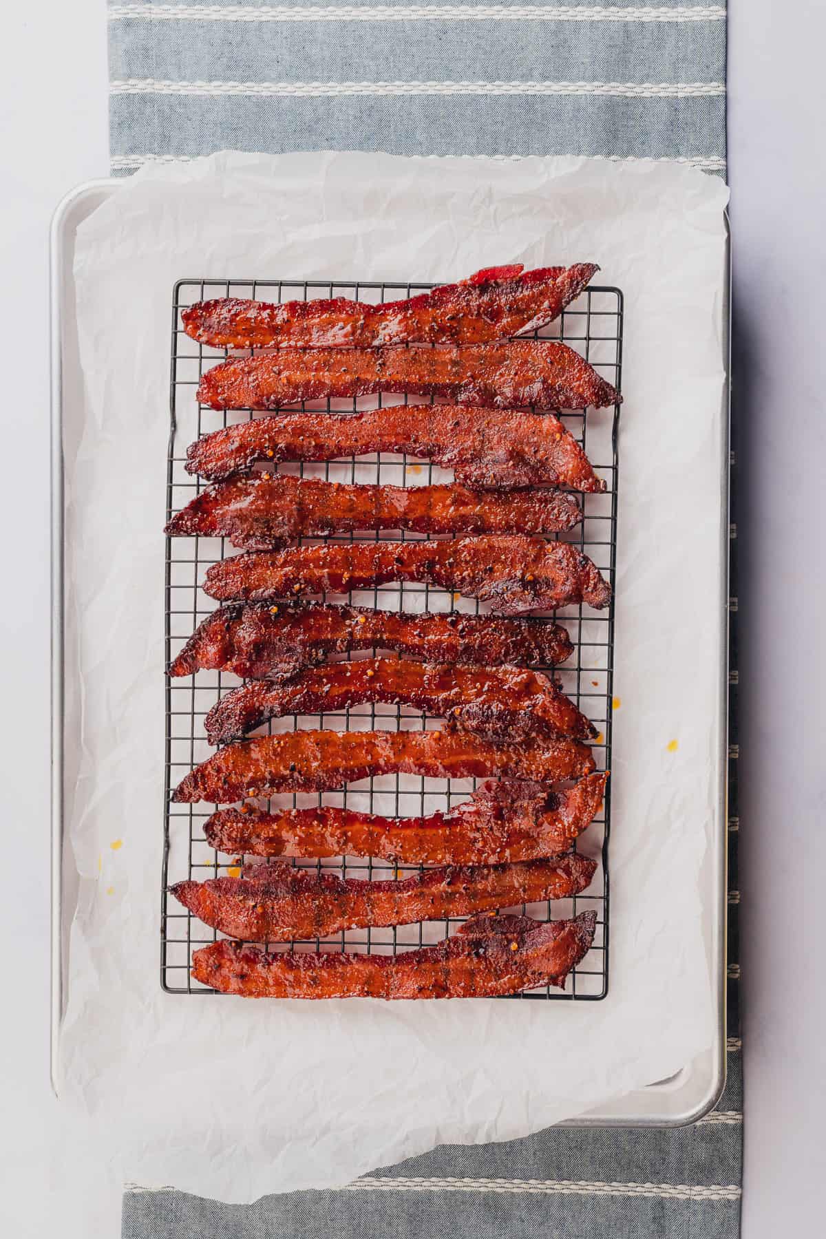 billionaire candied bacon on a wire cooling rack with parchment underneath on top of a baking sheet