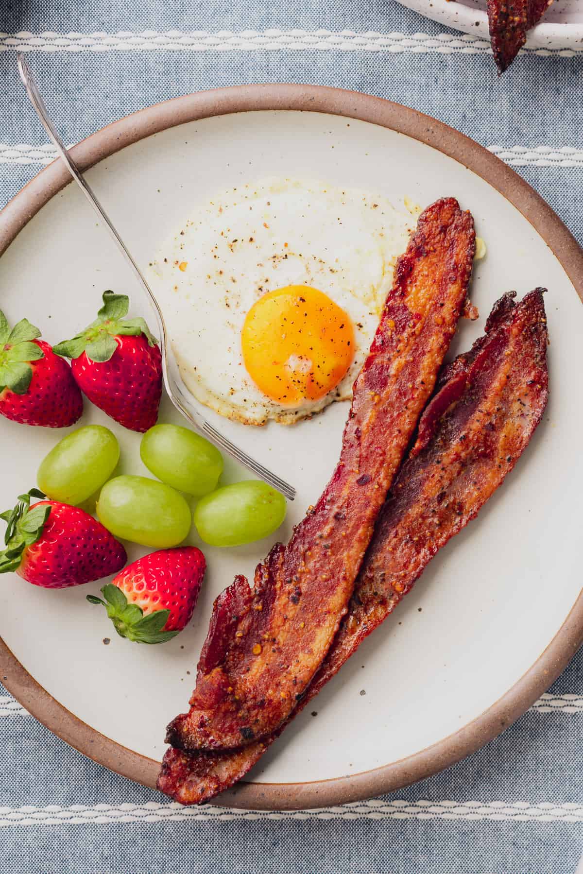 plate of keto candied bacon or billionaire bacon with fresh green grapes, strawberries, and a sunny side up egg 
