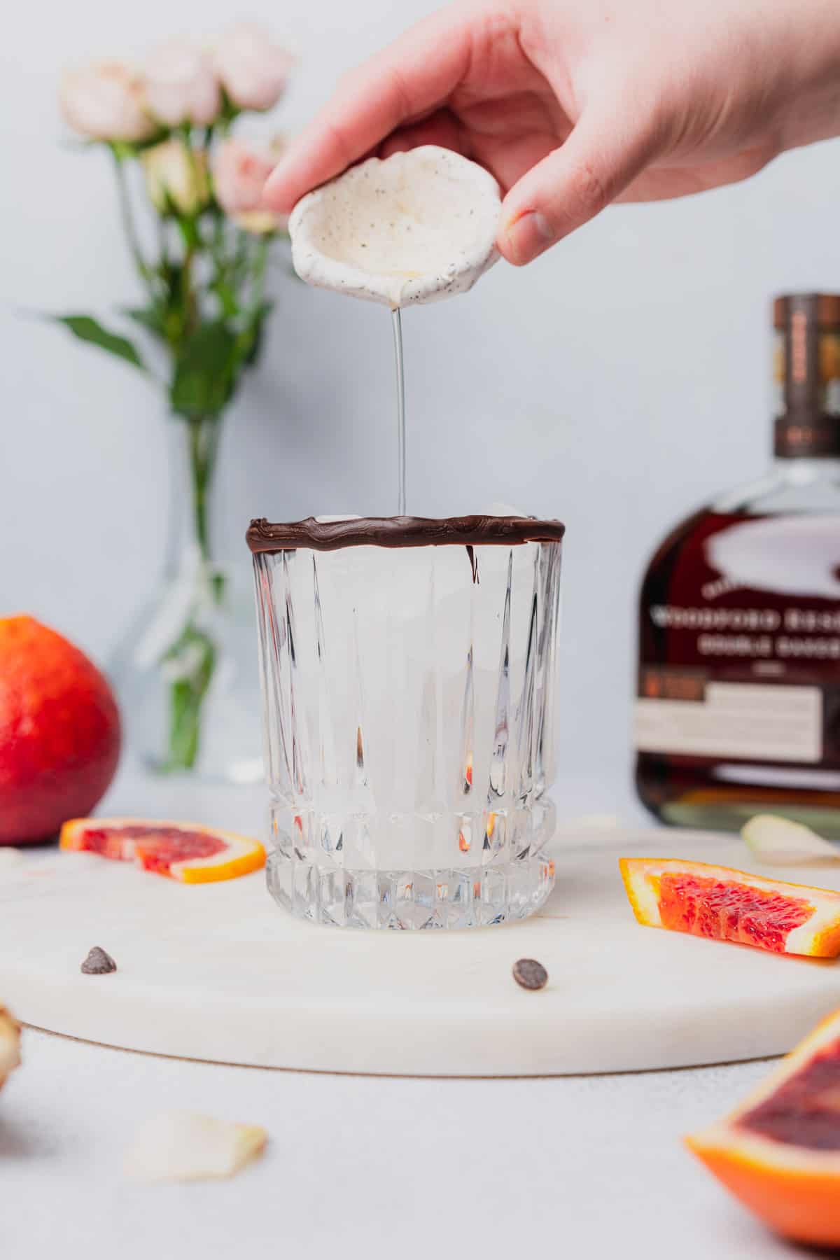 hand pouring orange bitters into a chocolate rimmed glass 